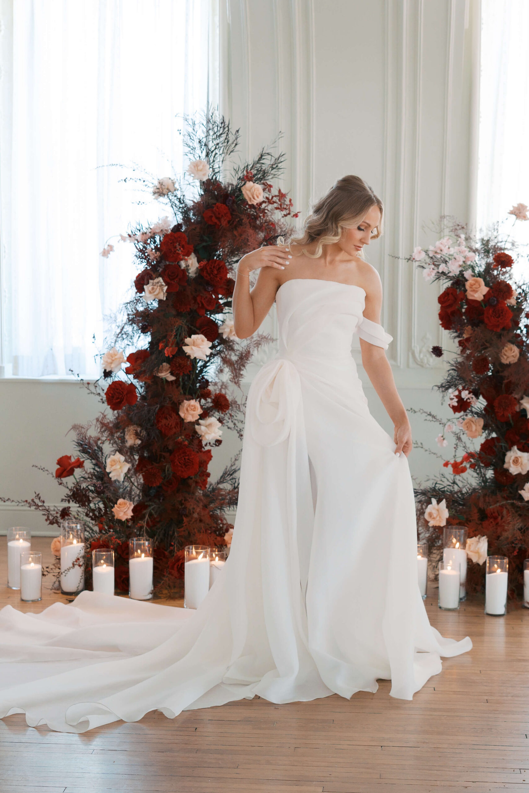A bride admires her gown while standing in front of two dark flower towers at her cottonwood hotel wedding