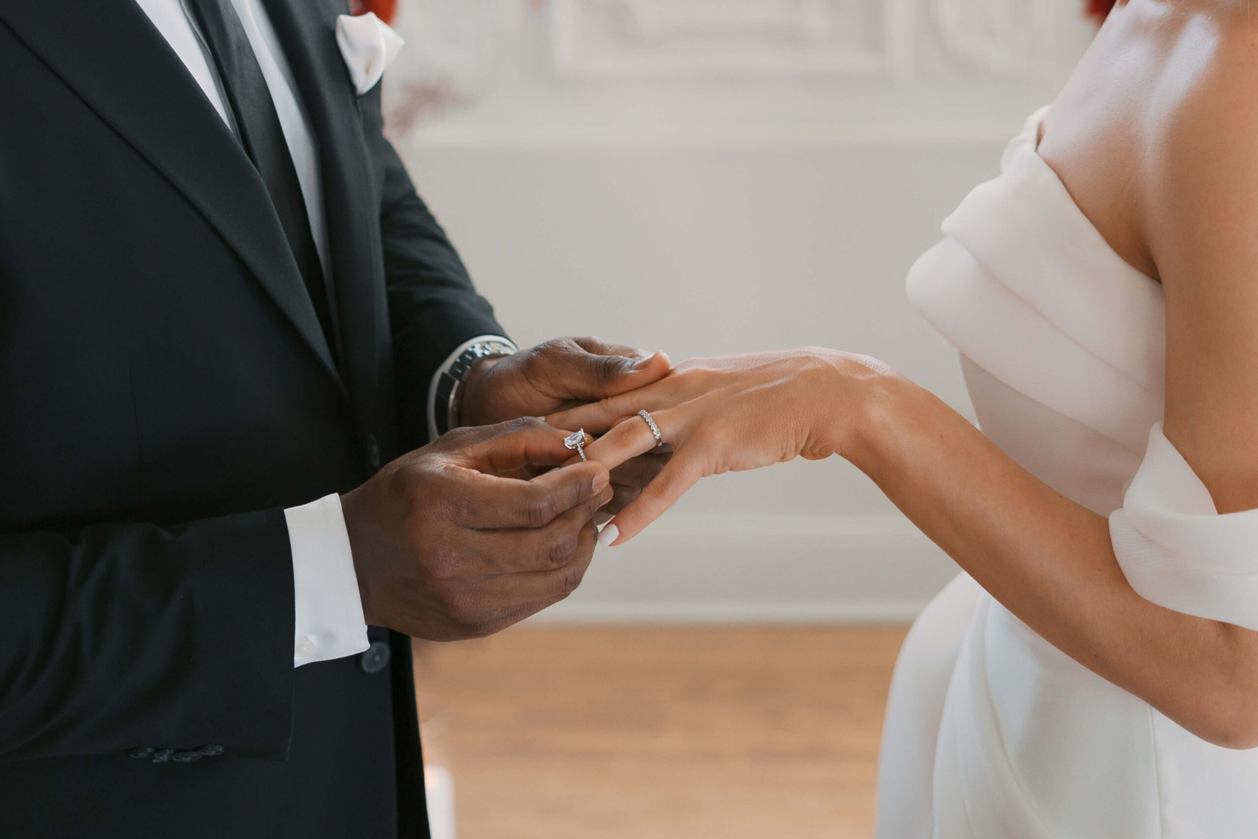 Details of a groom putting on the bride's ring on her finger during their indoor ceremony