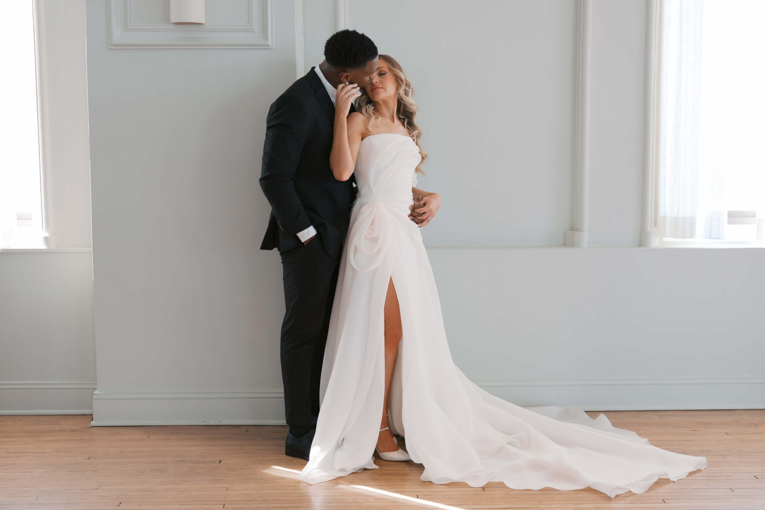 Newlyweds lean in for a snuggled kiss against a wall