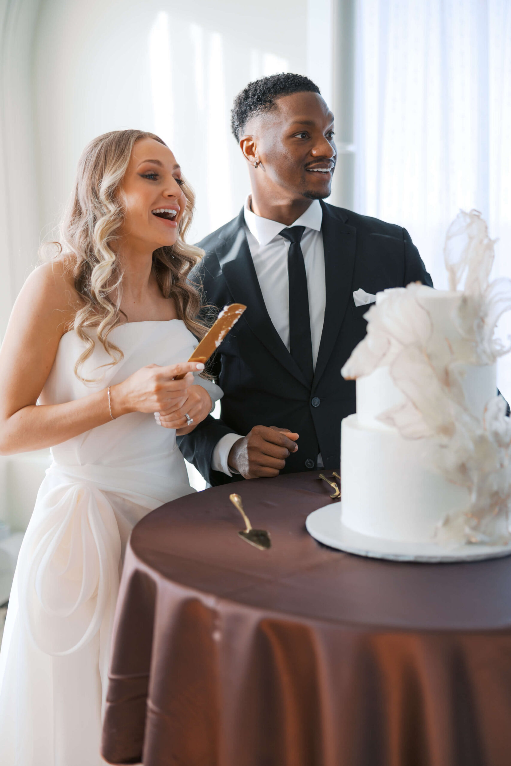 A b ride and groom smile while cutting their two tier cake during their cottonwood hotel wedding reception