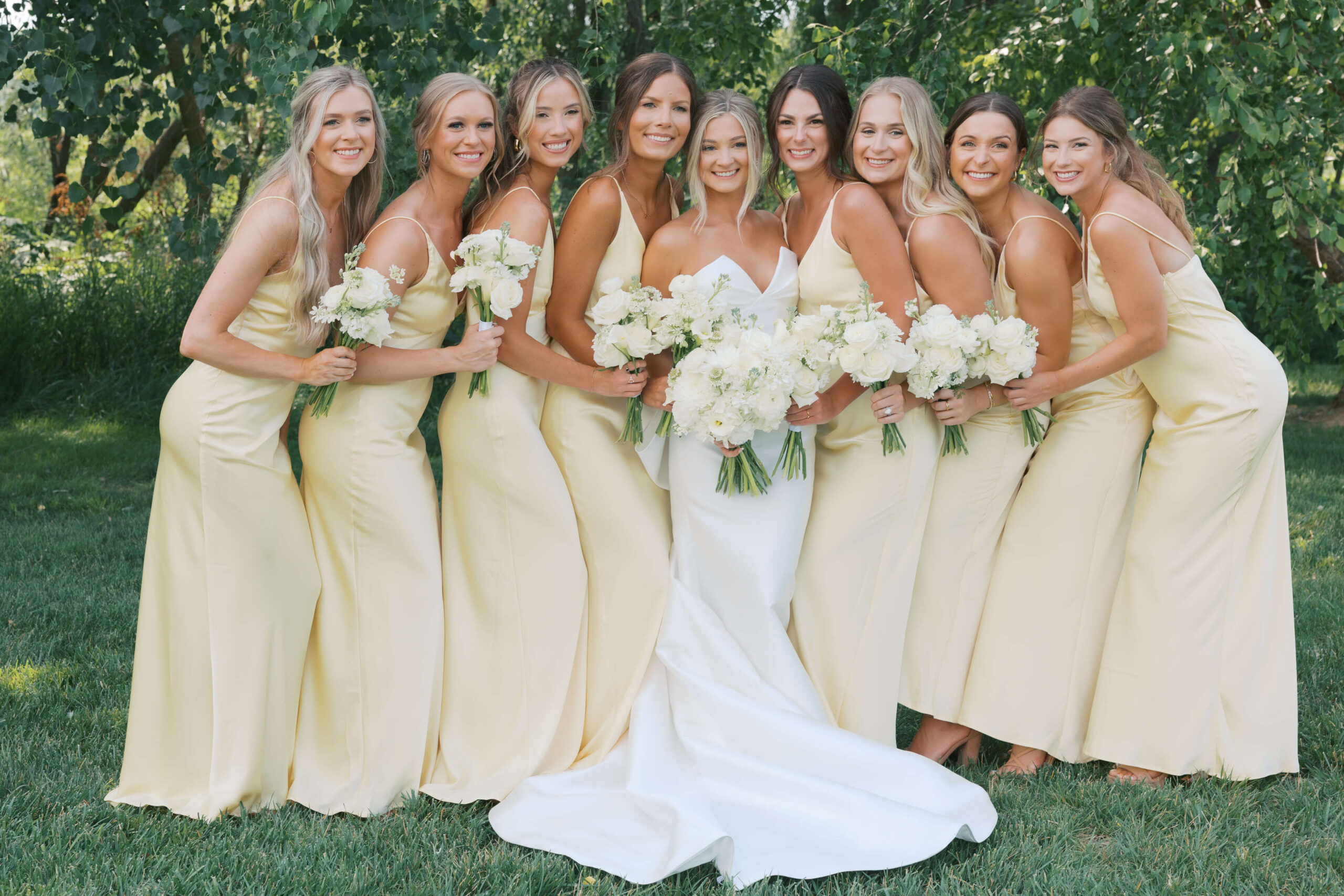 A happy bride smiles big with her bridesmaids in matching yellow gowns in a lawn during her happy hollow club omaha wedding