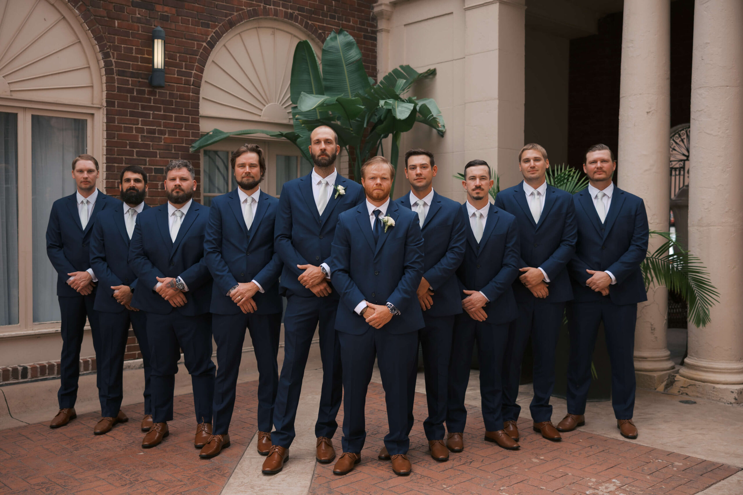 A groom in a blue suit stands with hands folded in front of him with his matching groomsmen