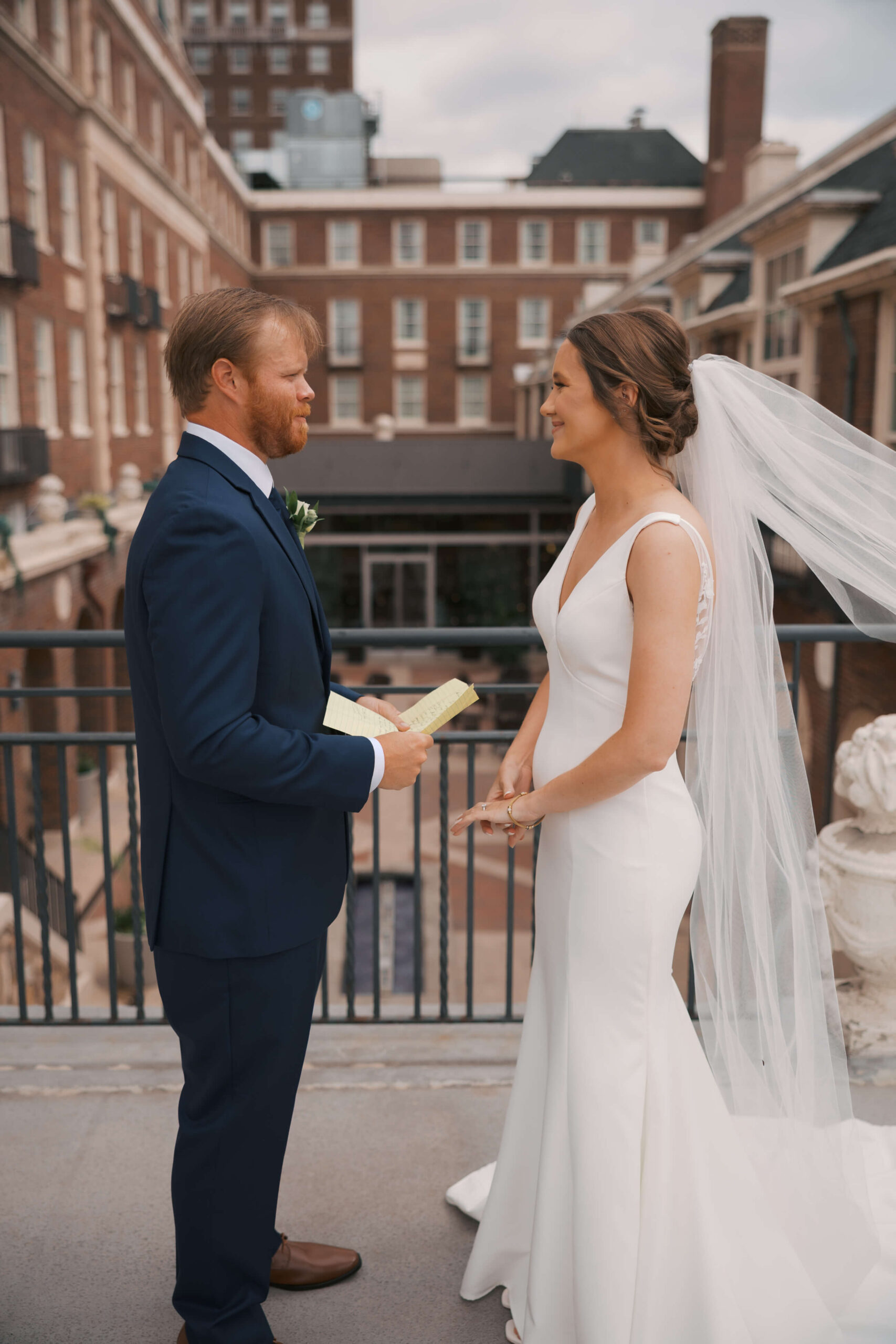 A groom reads a note to his bride as they stand on a balcony during their magnolia hotel wedding first look