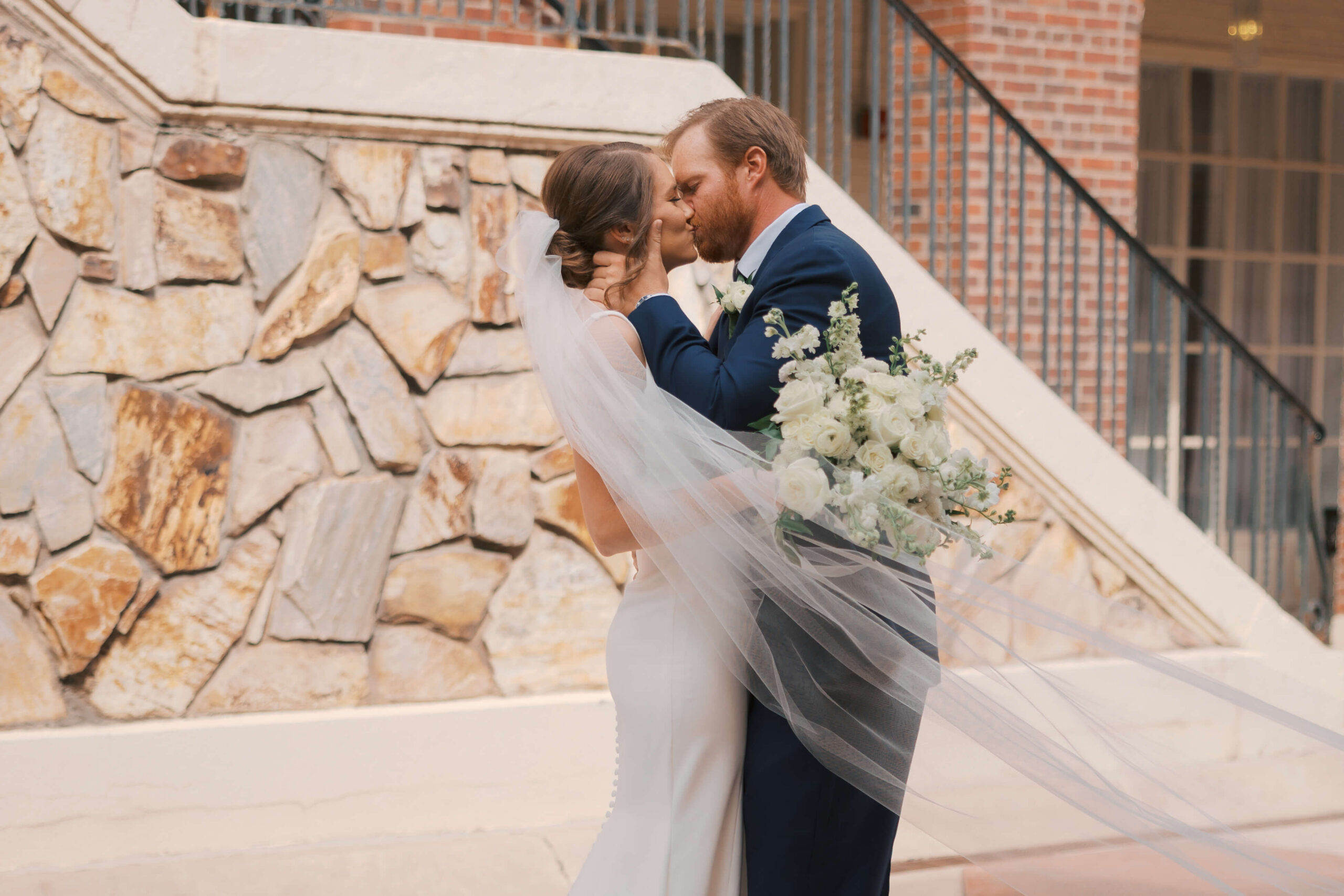 A bride and groom kiss as the veil blows around them in a patio