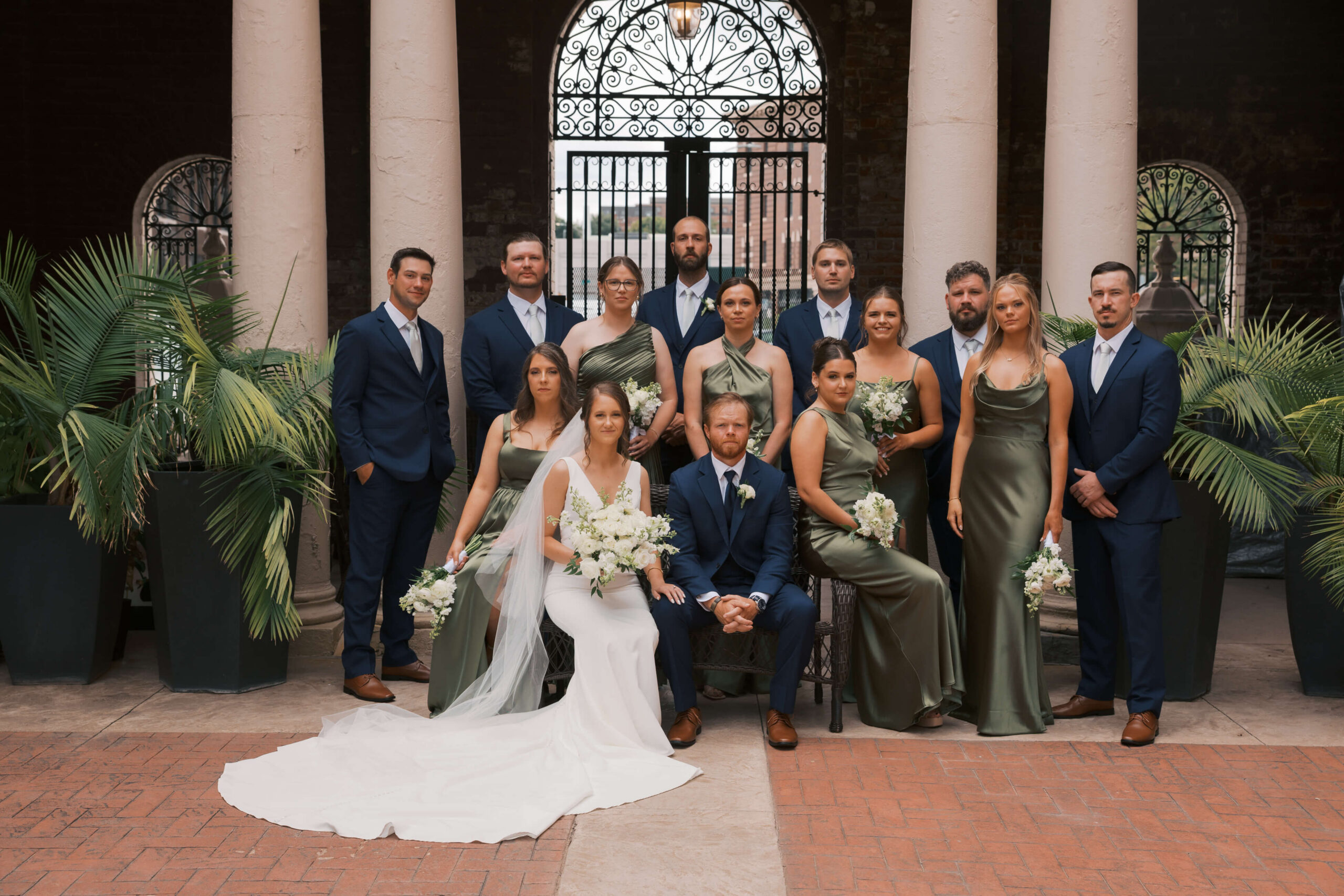 Newlyweds sit with their bridal party in green gowns and blue suits