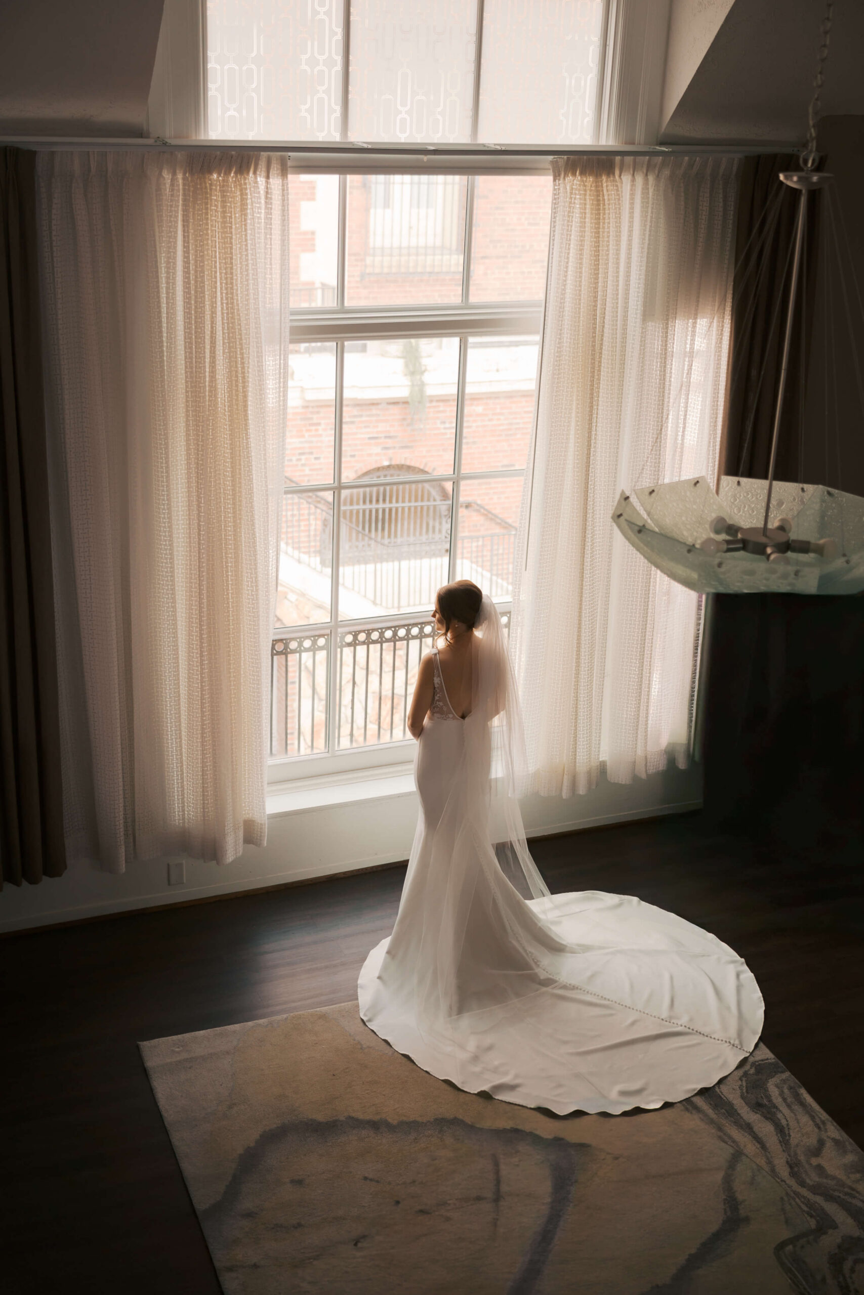 A look down from a balcony of a bride standing in a tall window in her gown at the magnolia hotel wedding venue
