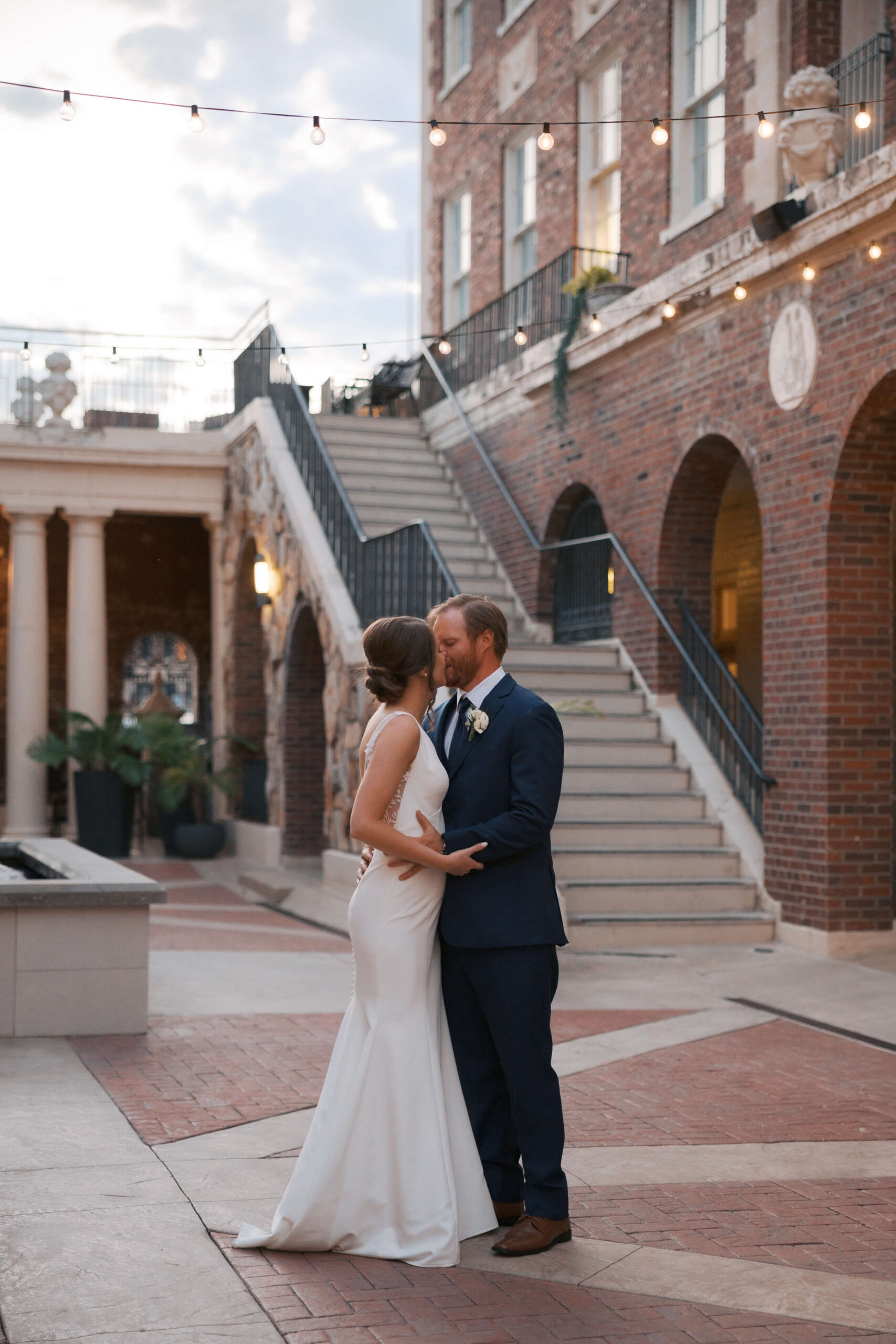 A bride and groom dance and kiss under market lights of a patio during their magnolia hotel wedding