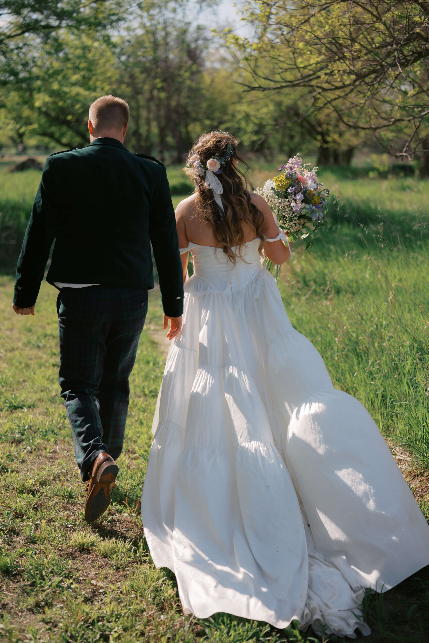 A bride and groom walk together in a trail at sunset holding the colorful bouquet