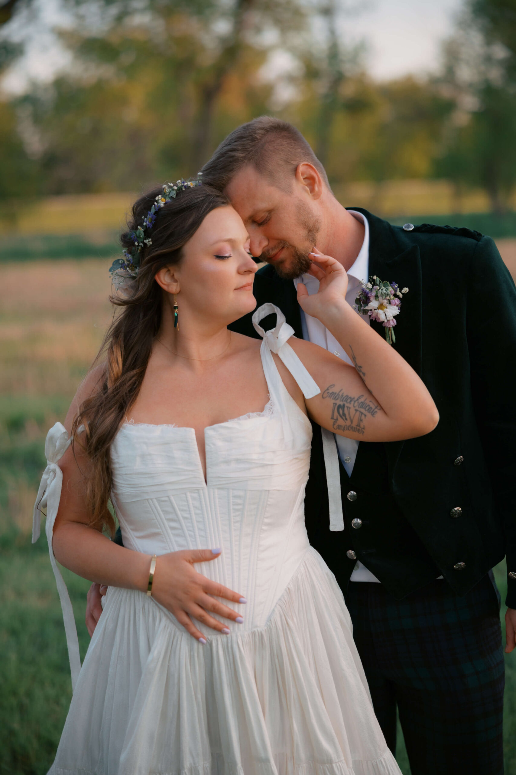 A bride leans into the chest of her groom as they stand in a lawn at sunset at the northern lights venue