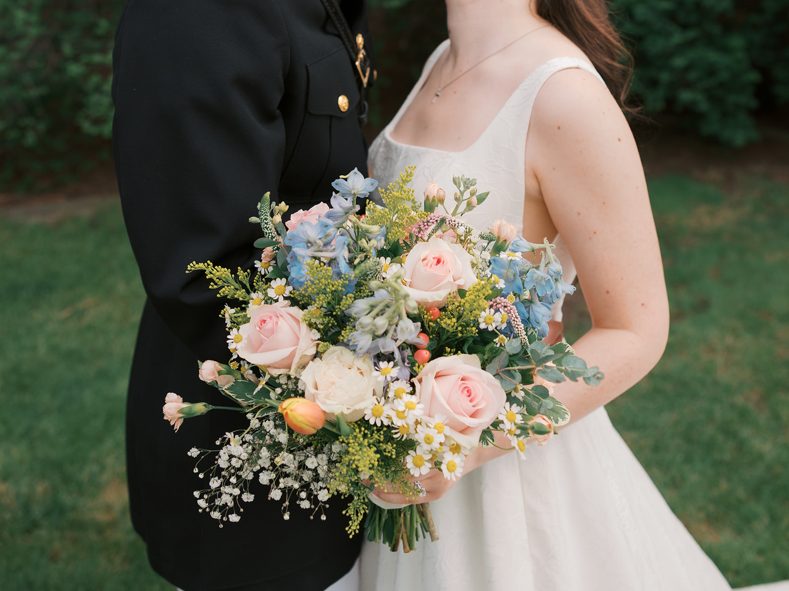 Details of a bride's colorful bouquet in her hand while standing with groom in lawn