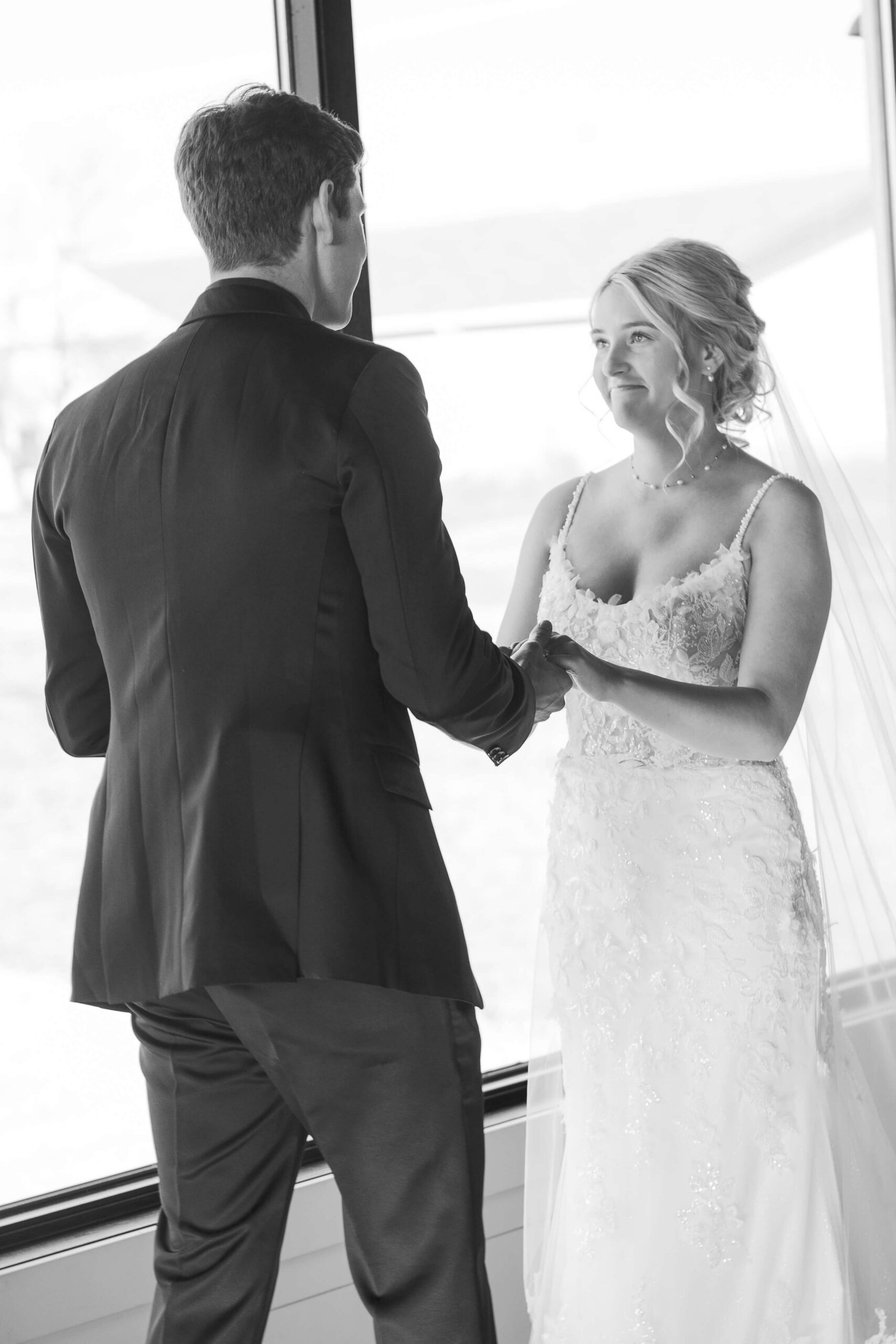 A bride almost cries during her first look holding hands with her groom in black and white on a balcony in a window at the Seven Willows wedding venue