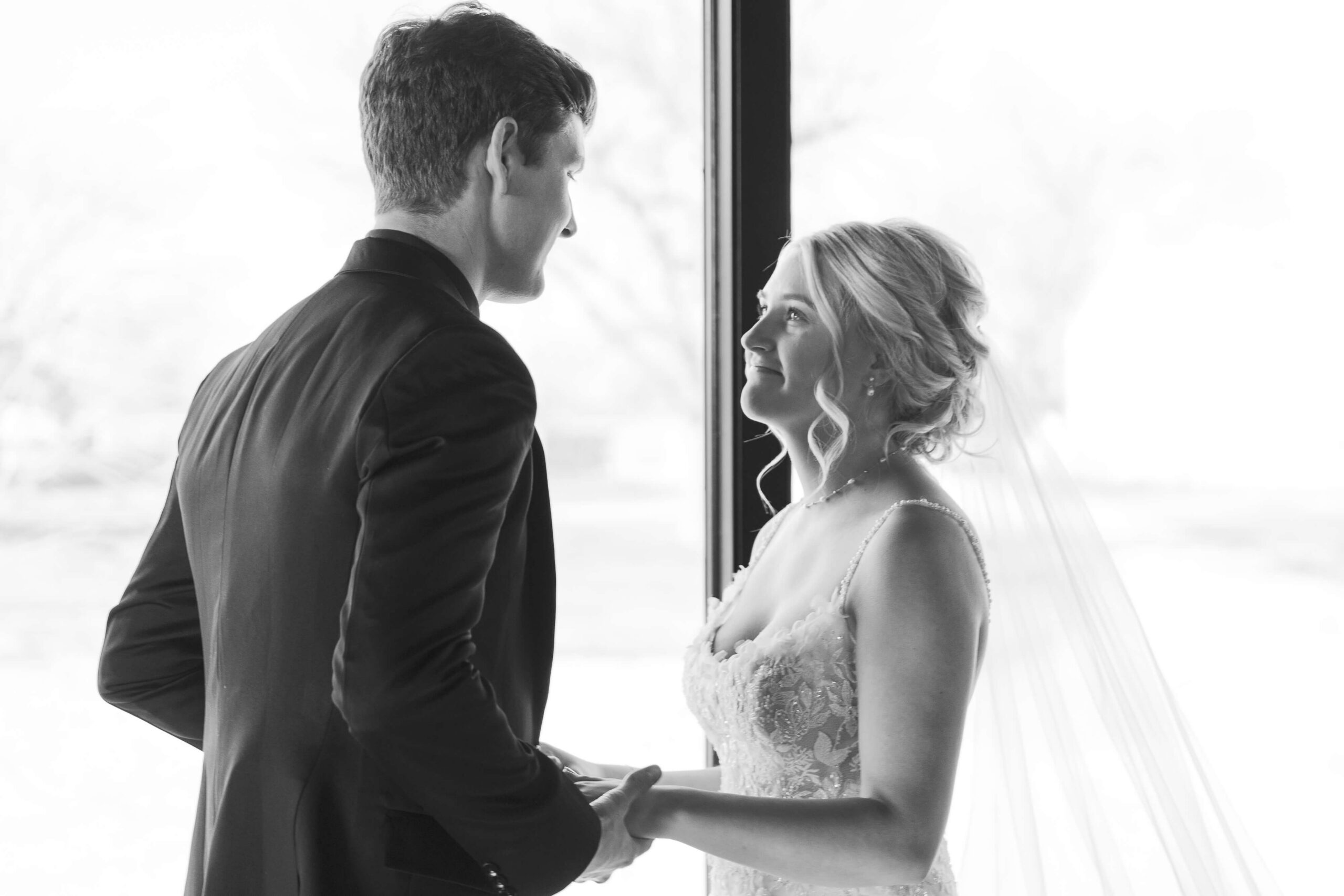 A bride smiles up to her groom while they hold hands in a window at the Seven Willows wedding venue