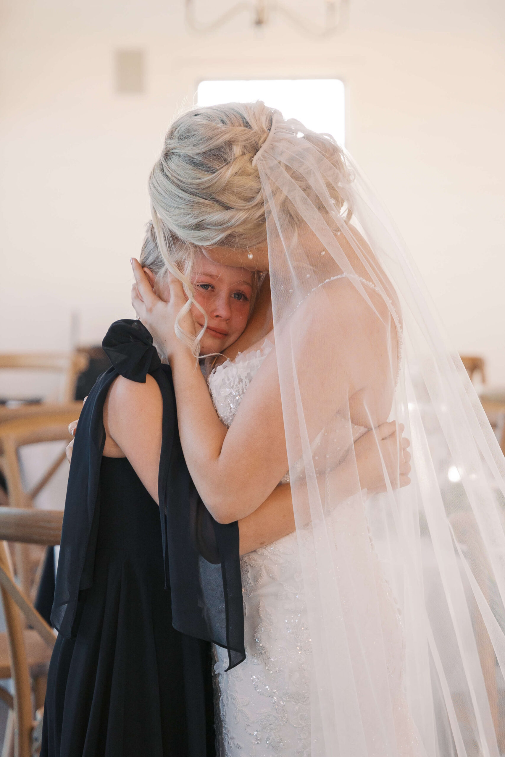 A young girl cries on the shoulder of a bride hugging her
