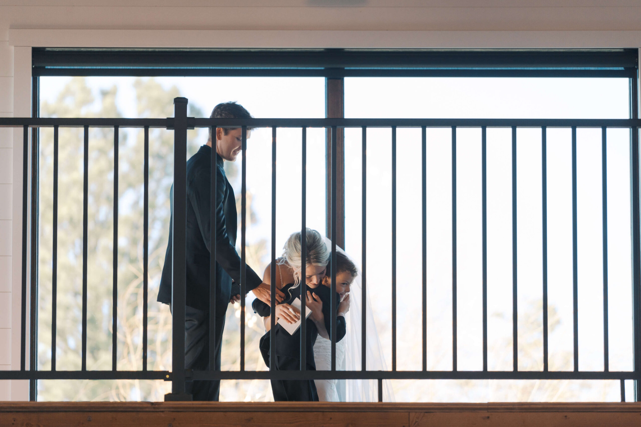 A bride hugs her son on a balcony with the groom at the Seven Willows wedding venue