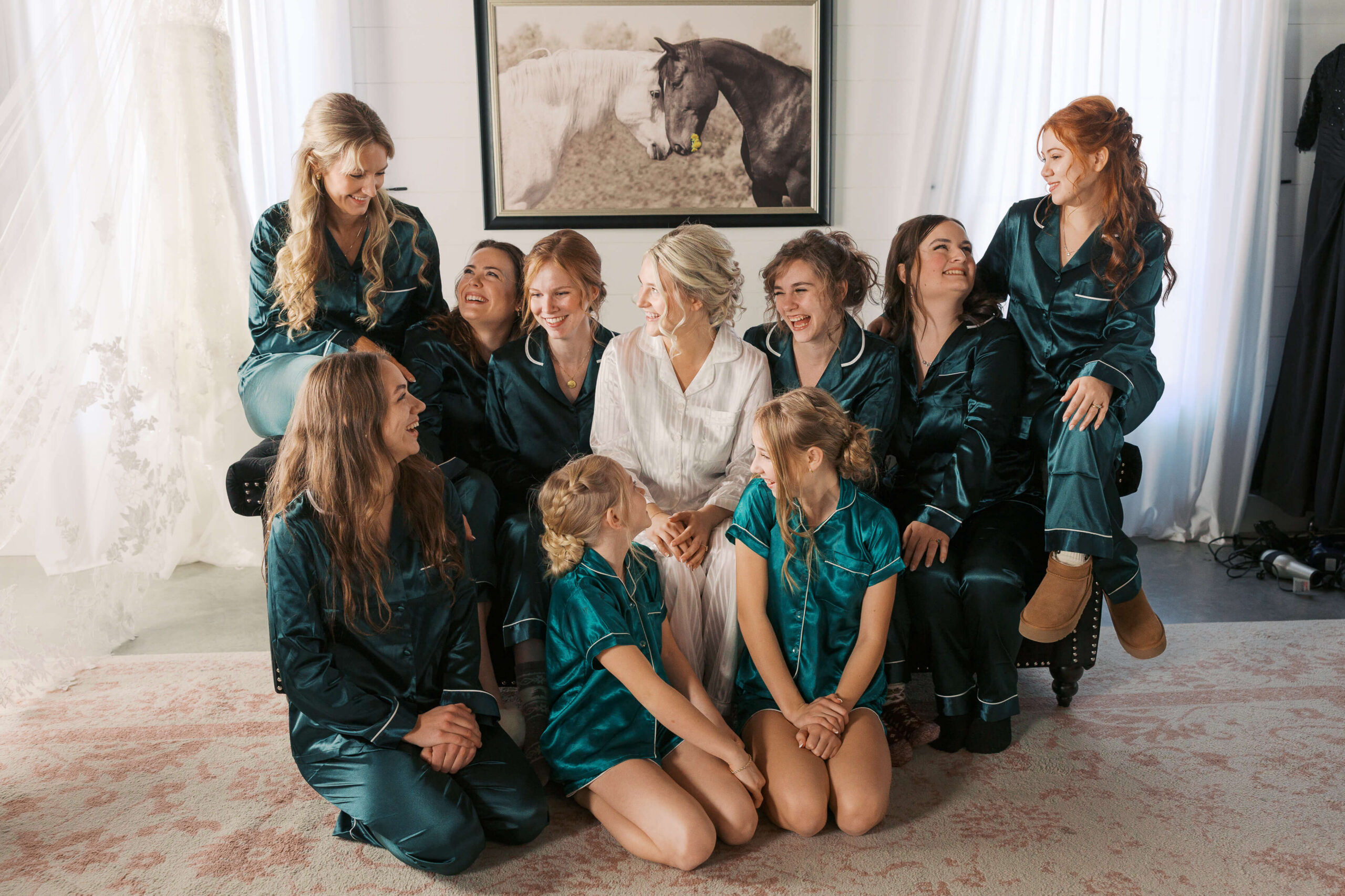 A bride laughs with her bridesmaids in matching green pajamas while sitting on a couch