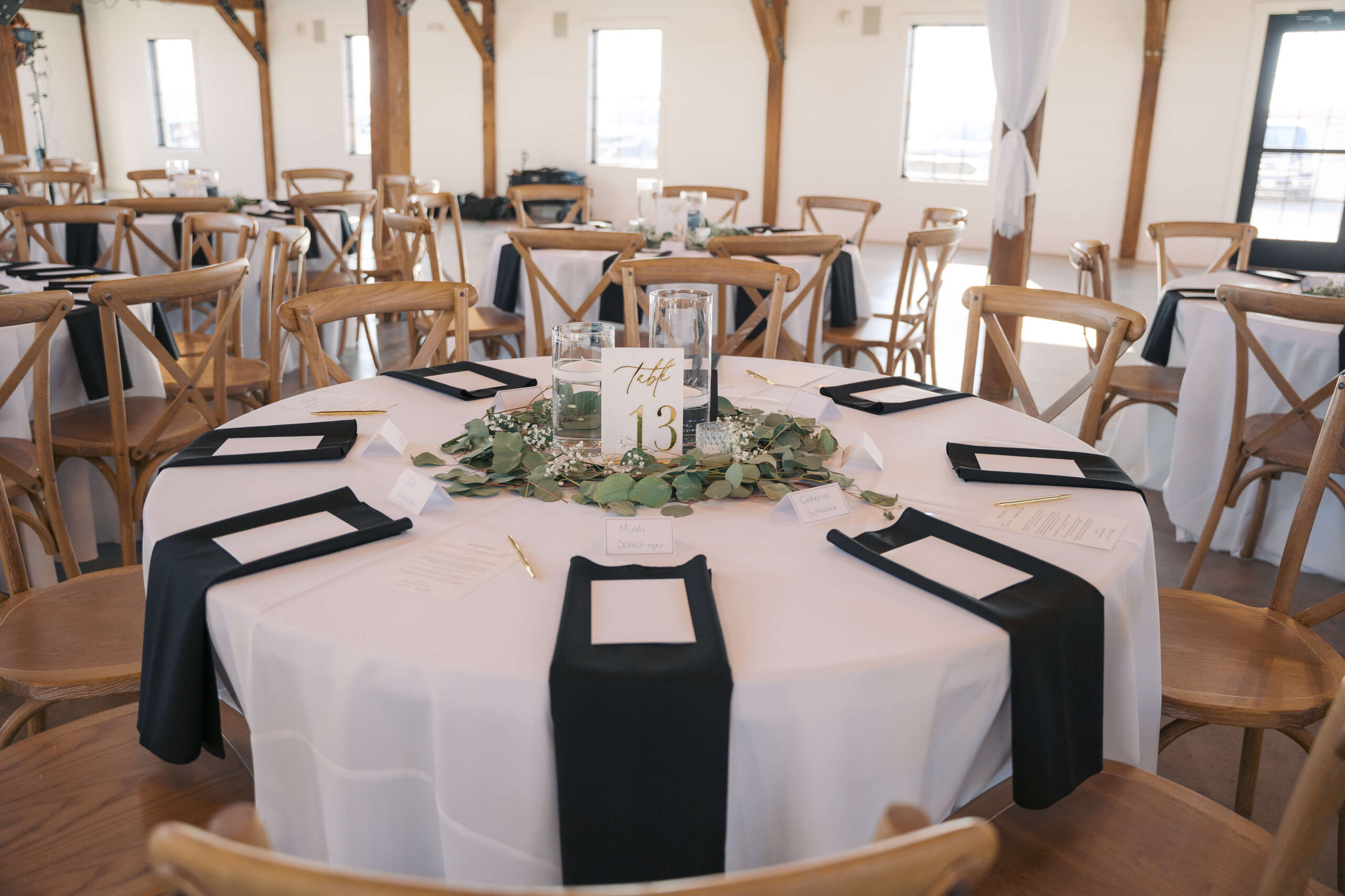 Details of a round wedding reception table with white linen, black napkins and wooden chairs