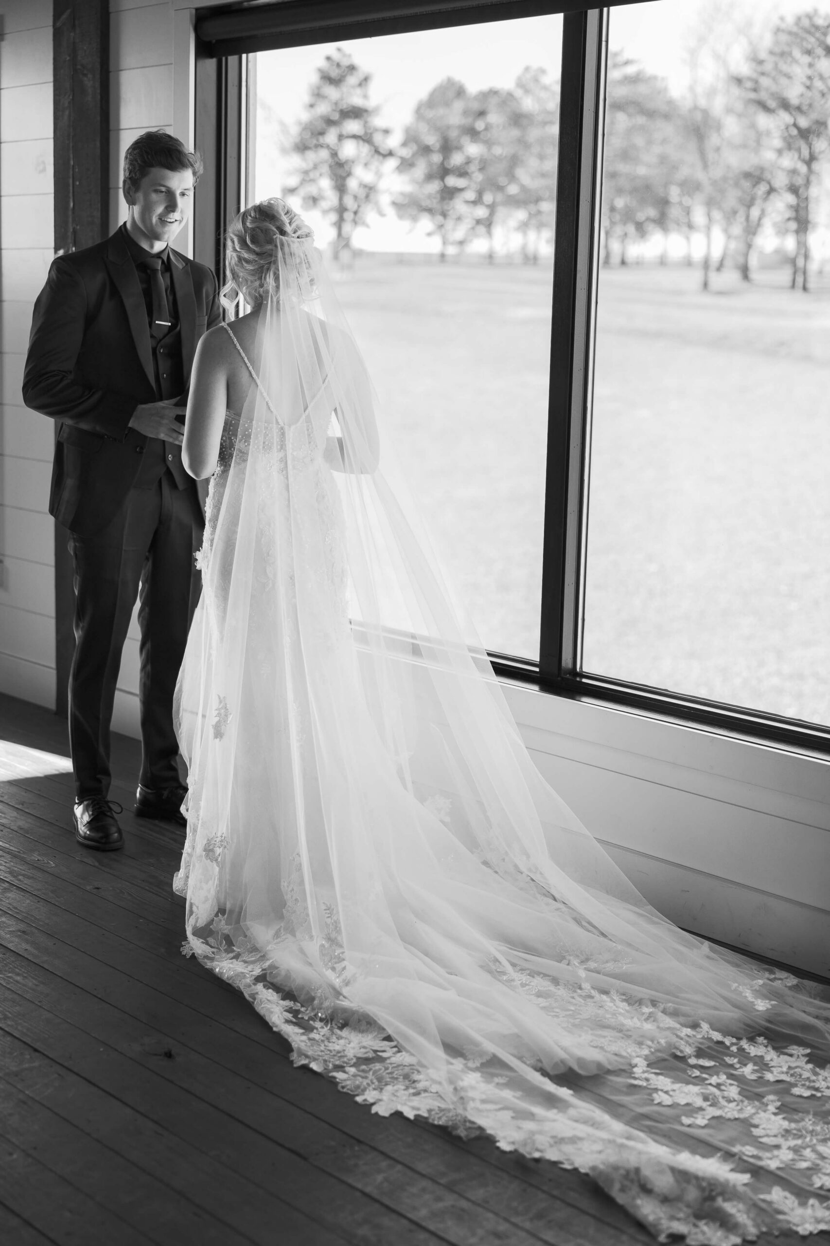 A bride and groom chat in a window during their first look at Seven Willows wedding venue
