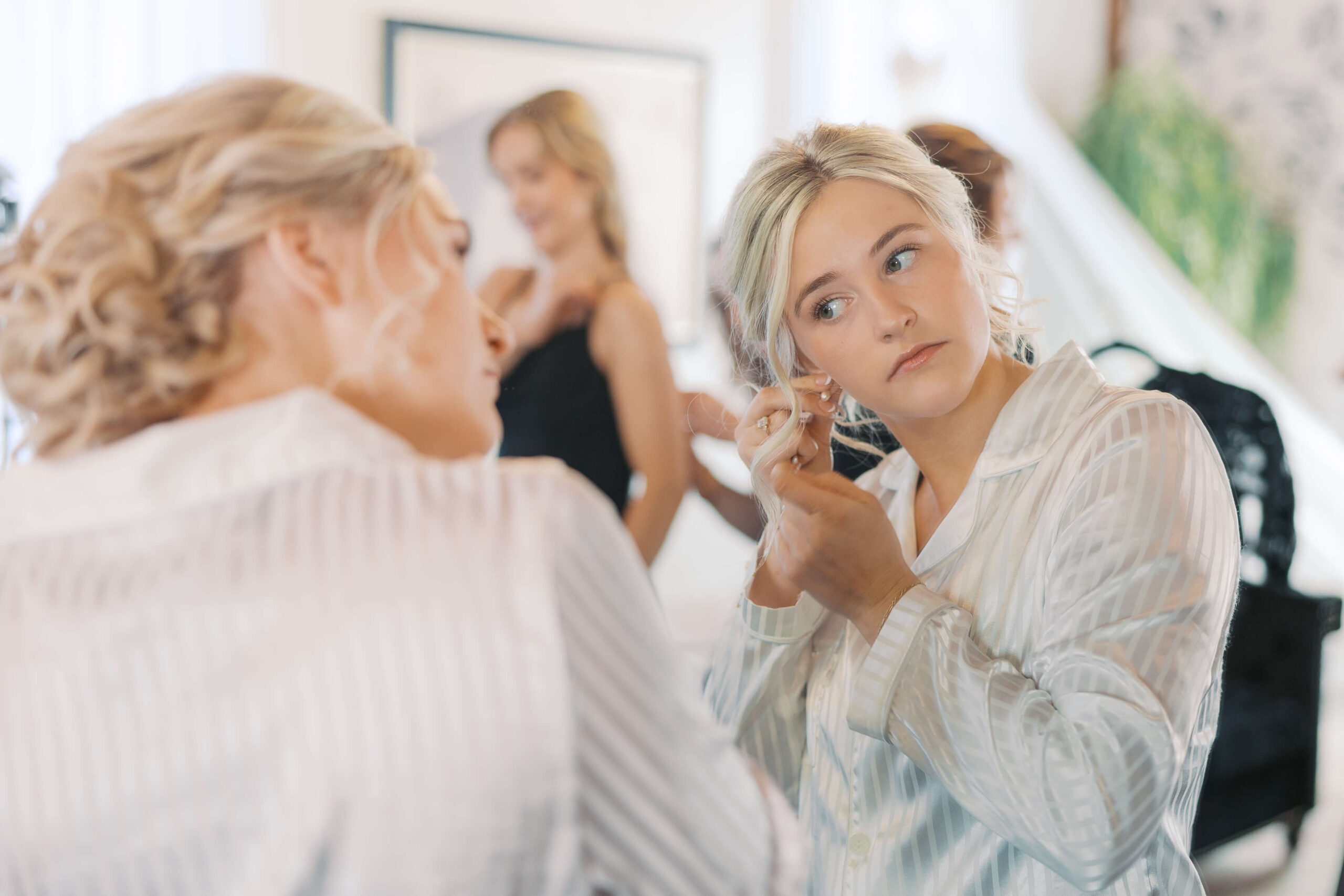A bride in white pajamas puts on her earrings in the getting ready suite