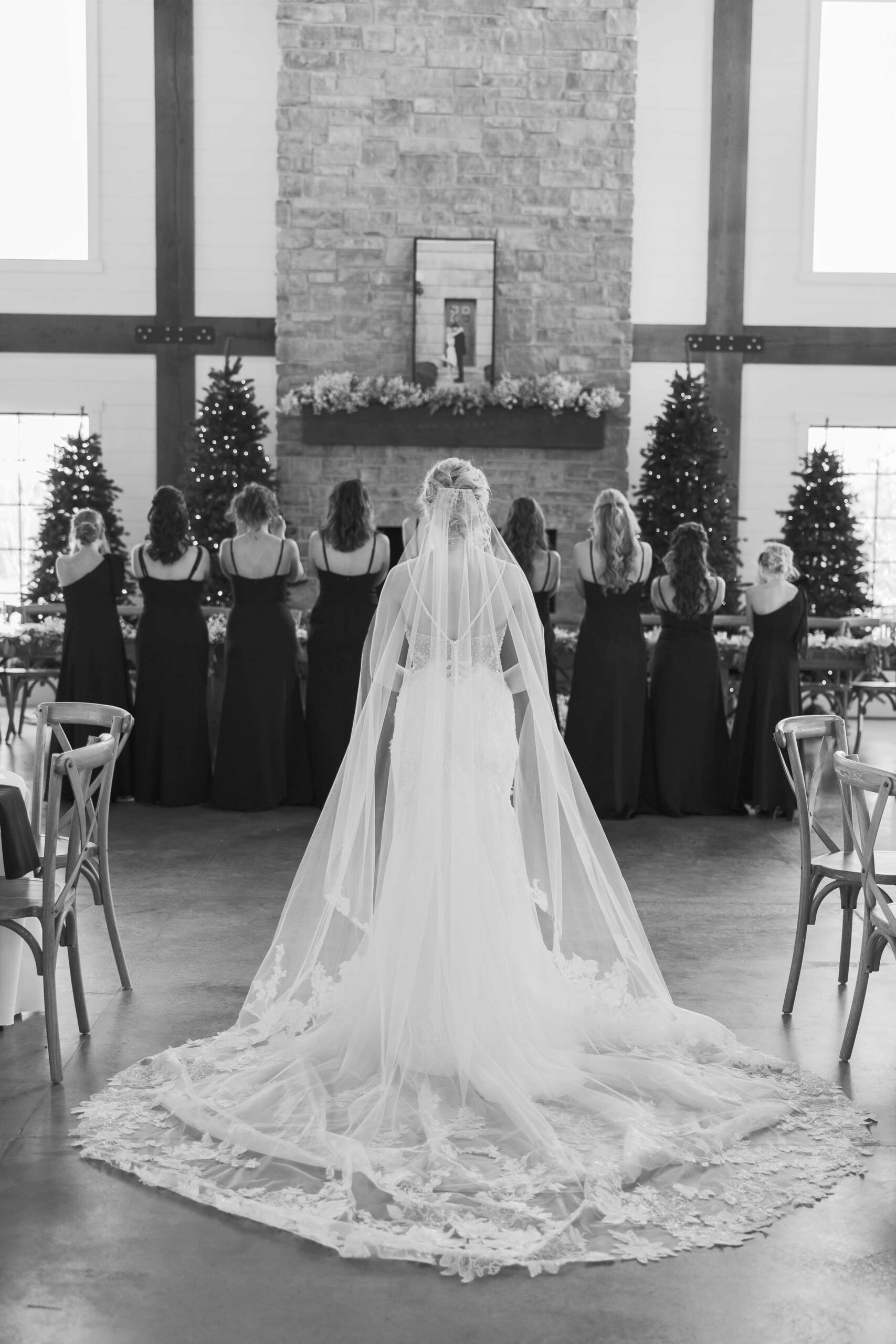 A bride stands with her train and veil spread as bridesmaids stand facing away in the reception space at the Seven Willows wedding venue