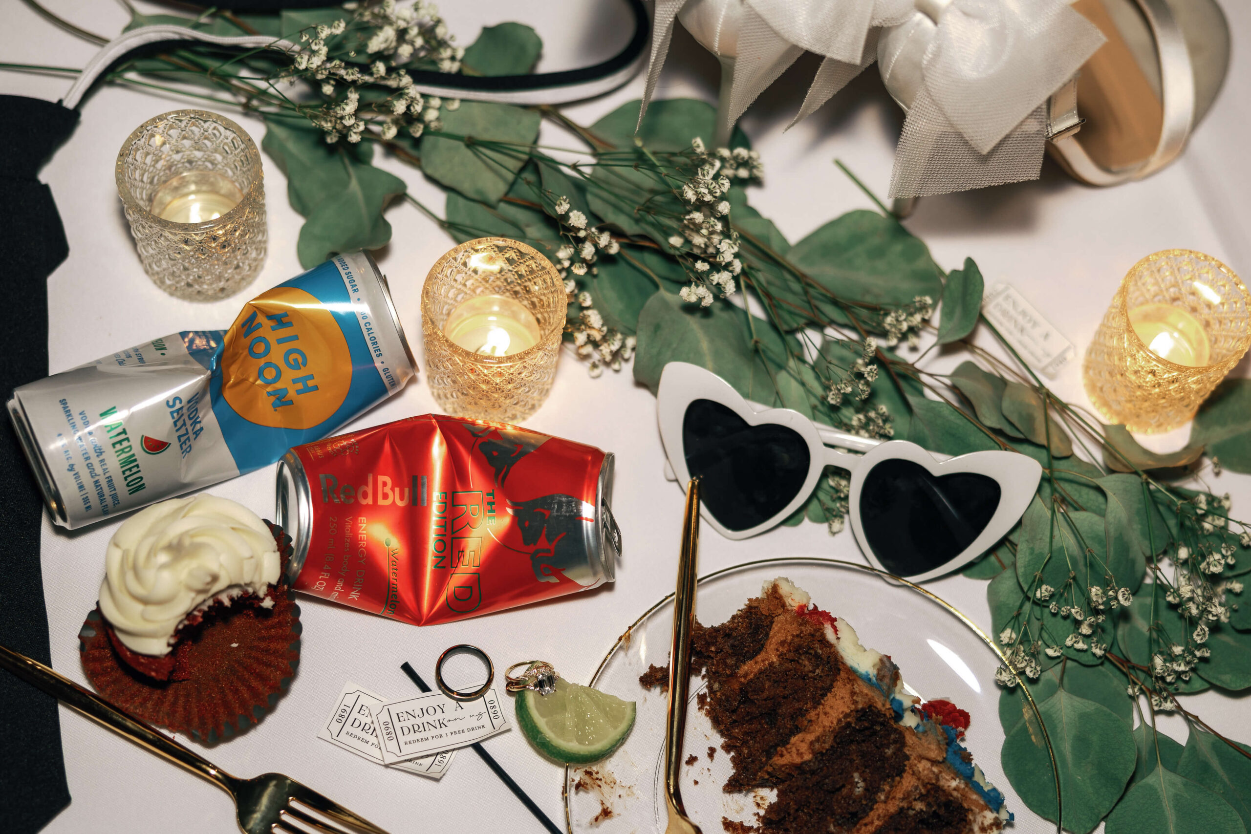 Details of sunglasses, wedding rings, crushed drink cans and cake on a reception table