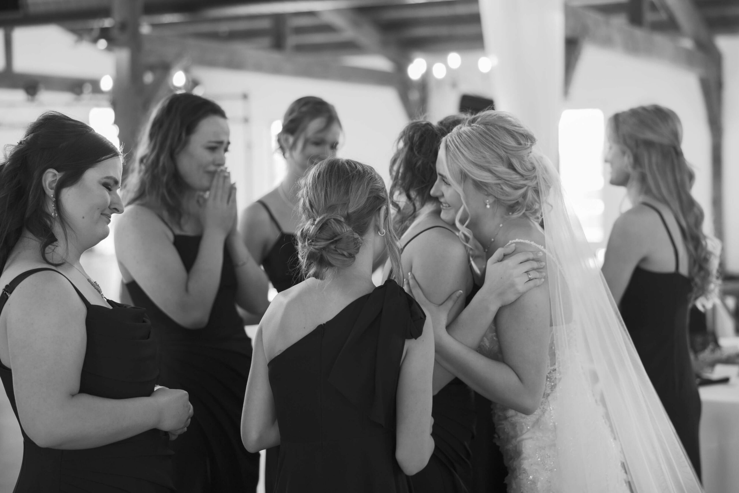 A happy bride hugs and smiles with her emotional bridesmaids seeing her in her gown for the first time at Seven Willows wedding venue