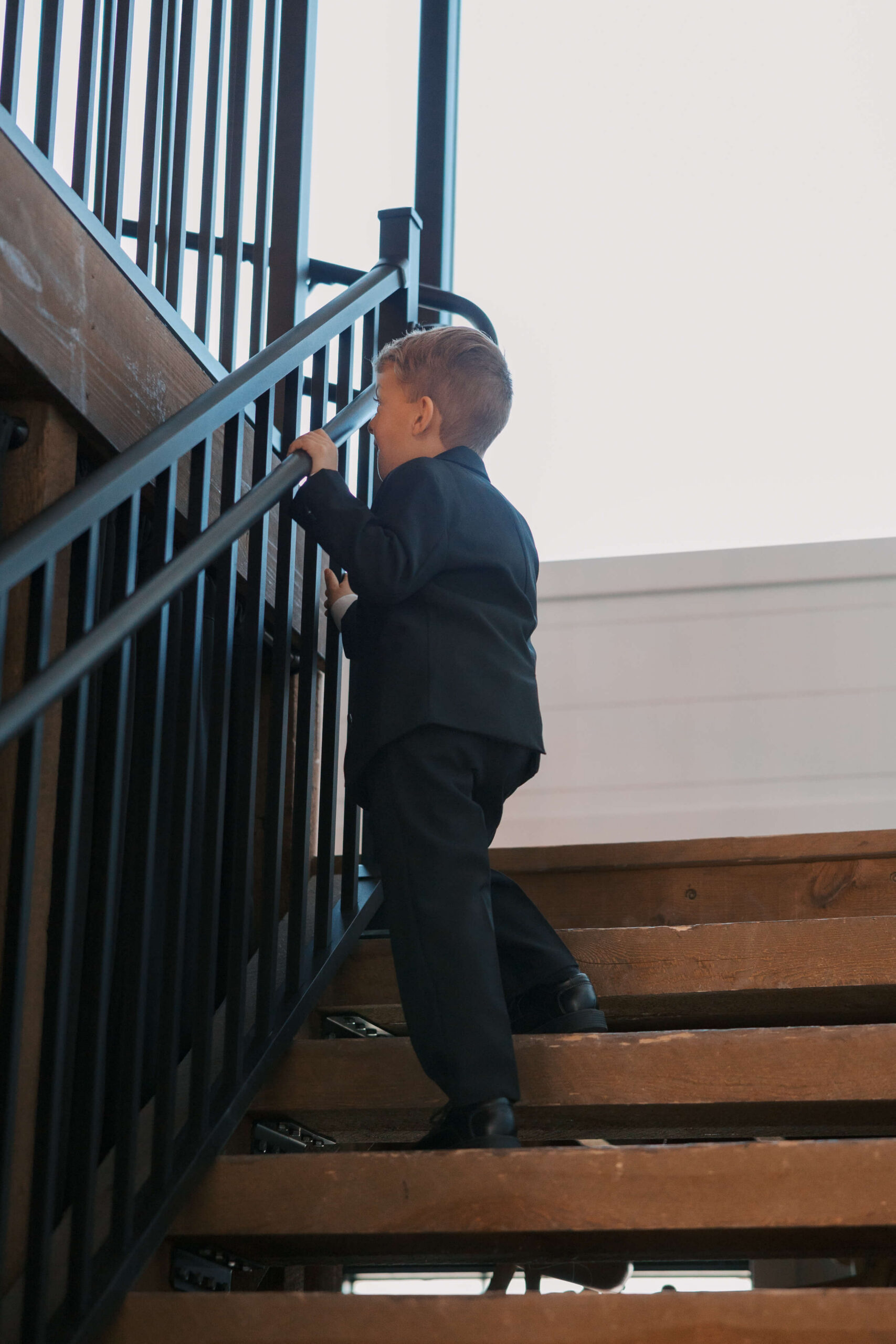 A child in a black suit peeks through the stairs