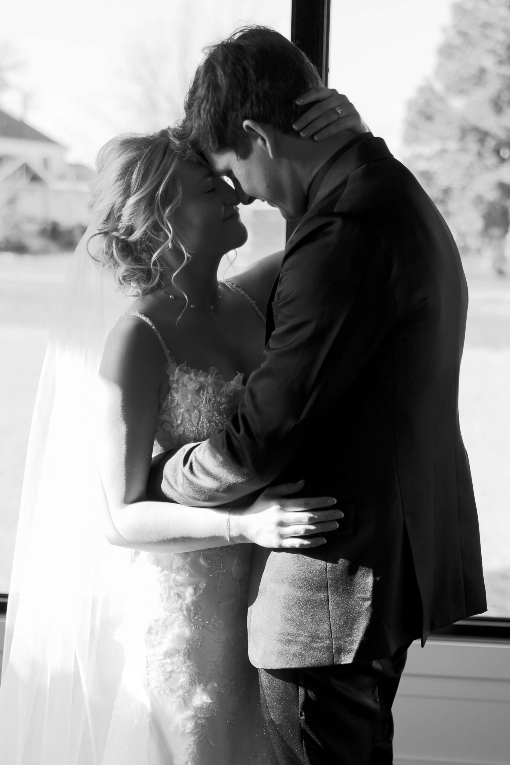 Happy newlywed couple snuggle close in a window in black and white