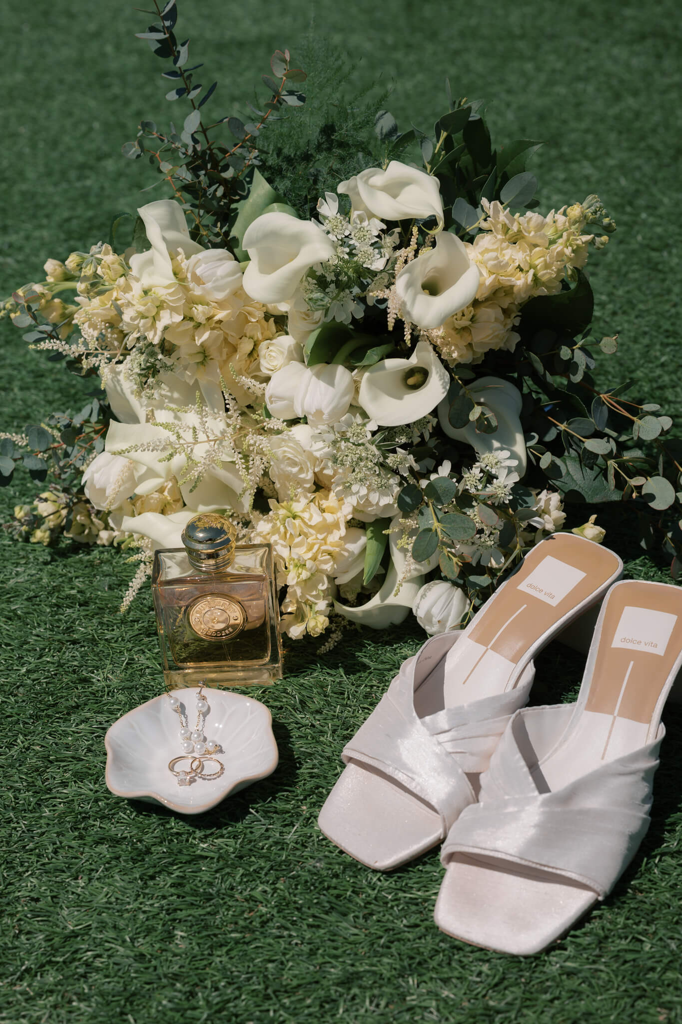 Bridal details on a lawn with shoes, bouquet, shell of jewelry and perfume