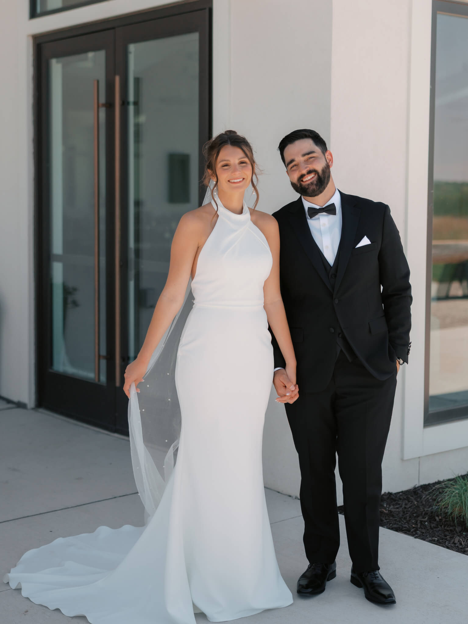 Happy newlyweds smile and hold hands while walking on a sidewalk