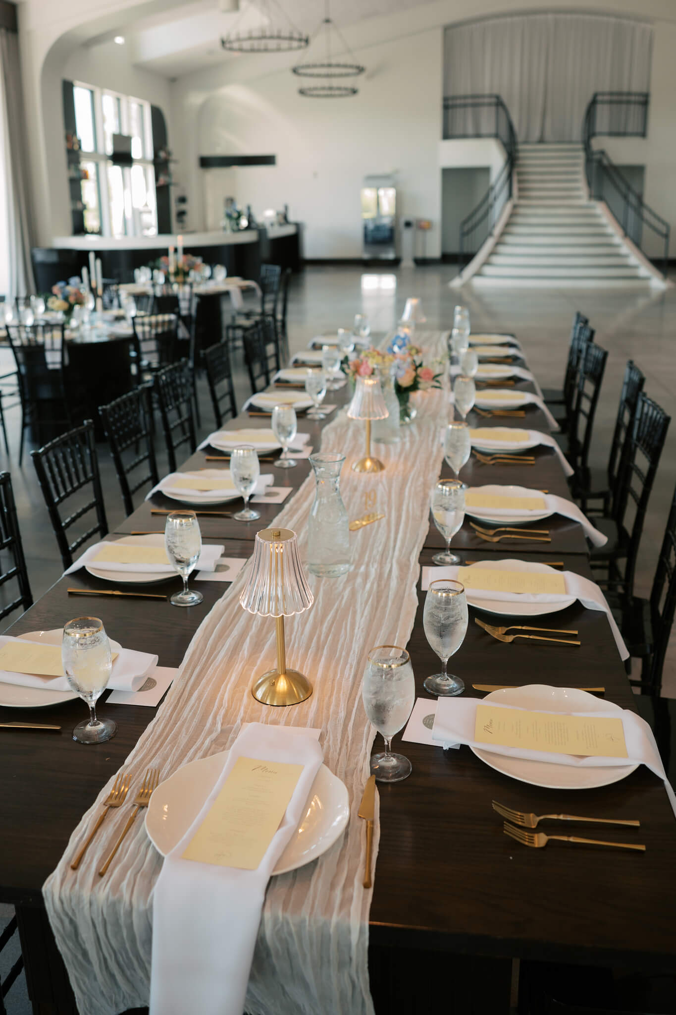 Details of a long wedding reception table set up atThe Acreage wedding venue ballroom with gold silverware and black chairs