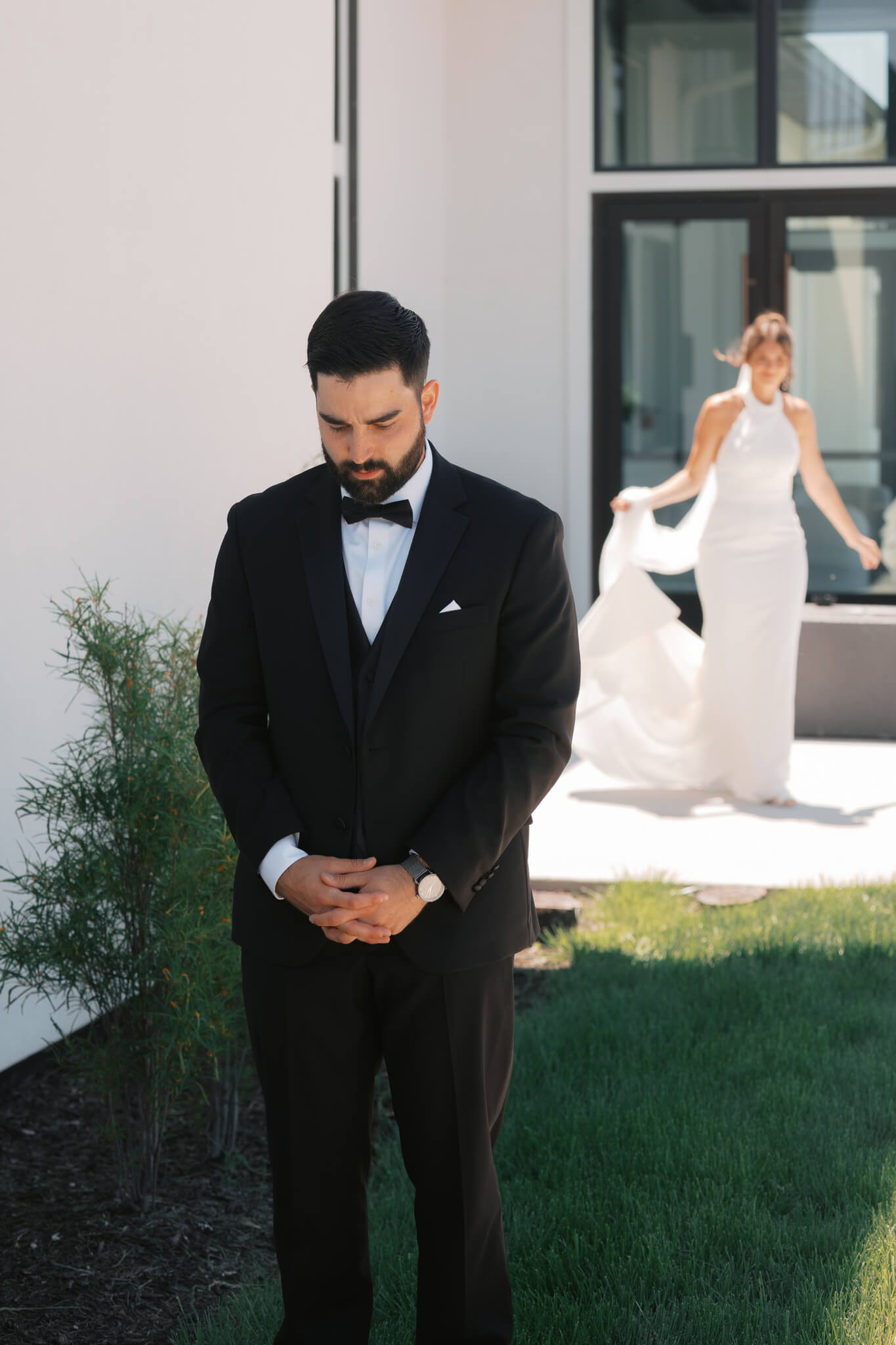 A groom anxiously awaits his bride to arrive for their first look in a garden