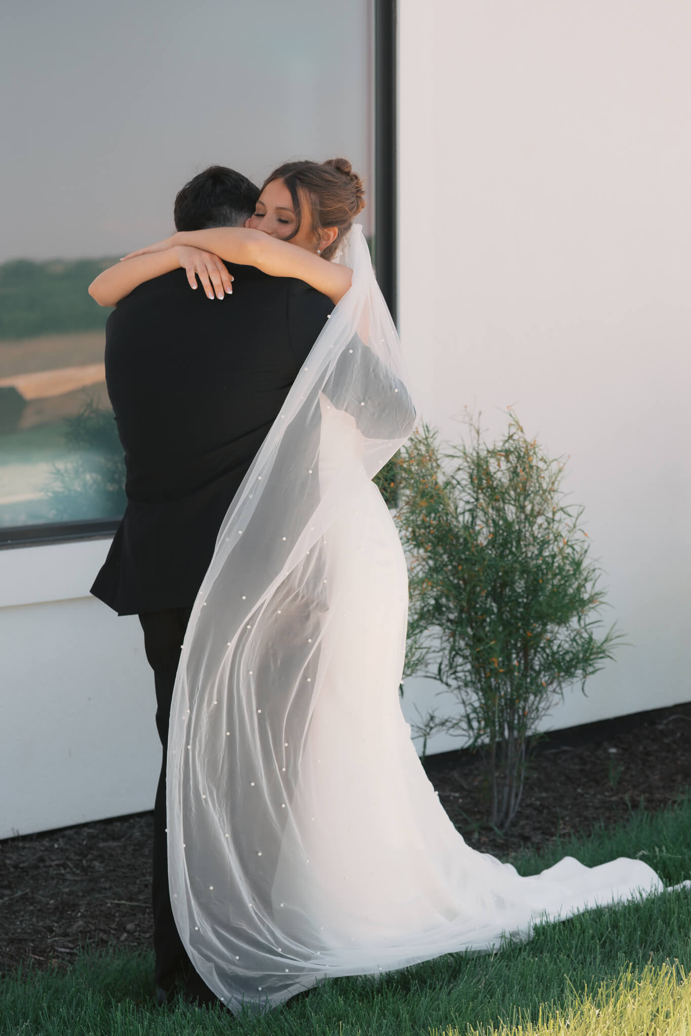 Happy bride and groom embrace as the veil wraps around them during their first look