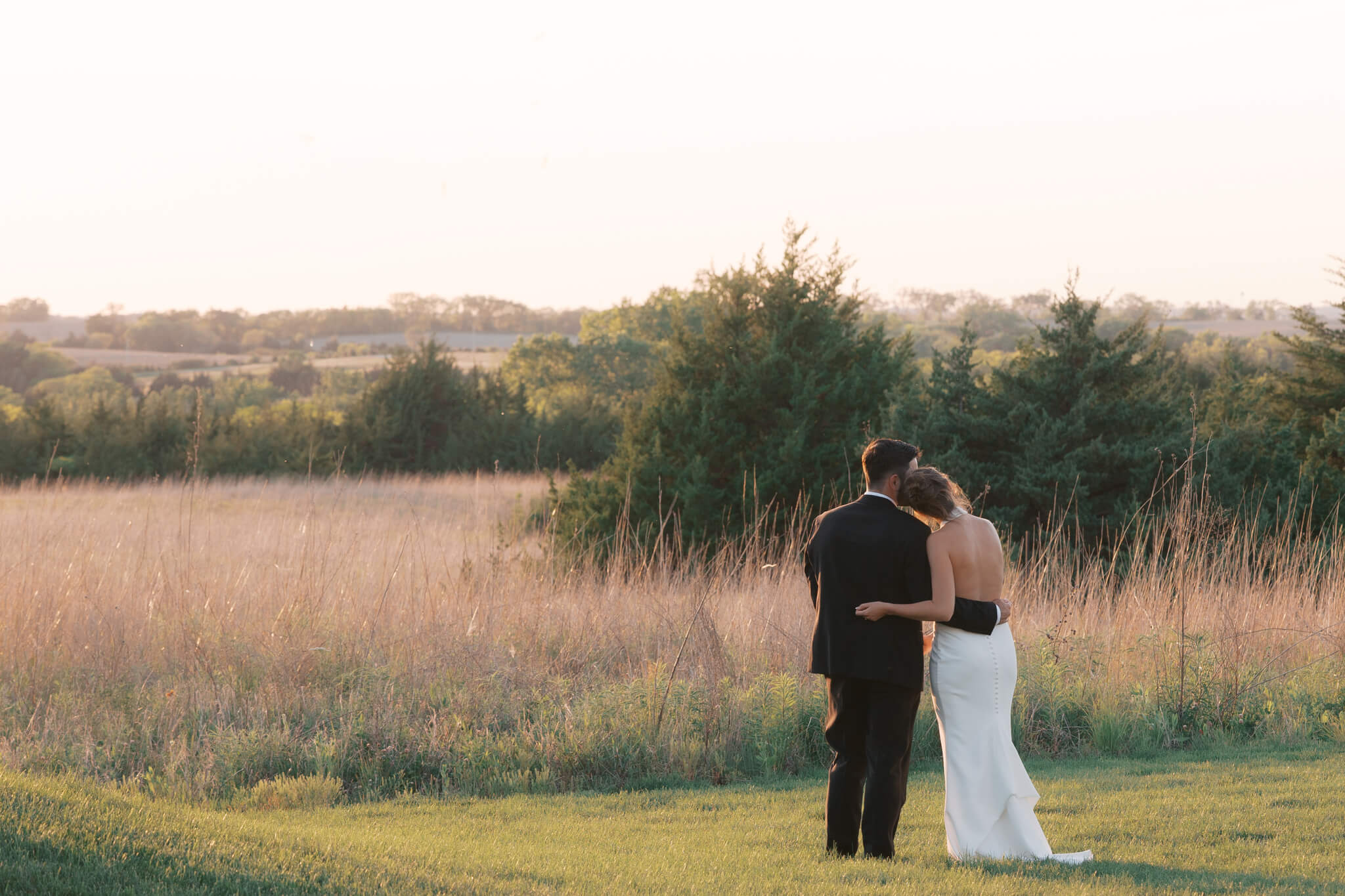 Newlyweds snuggle while enjoying The Acreage wedding venue sunset views over the rolling hills and tall golden grass