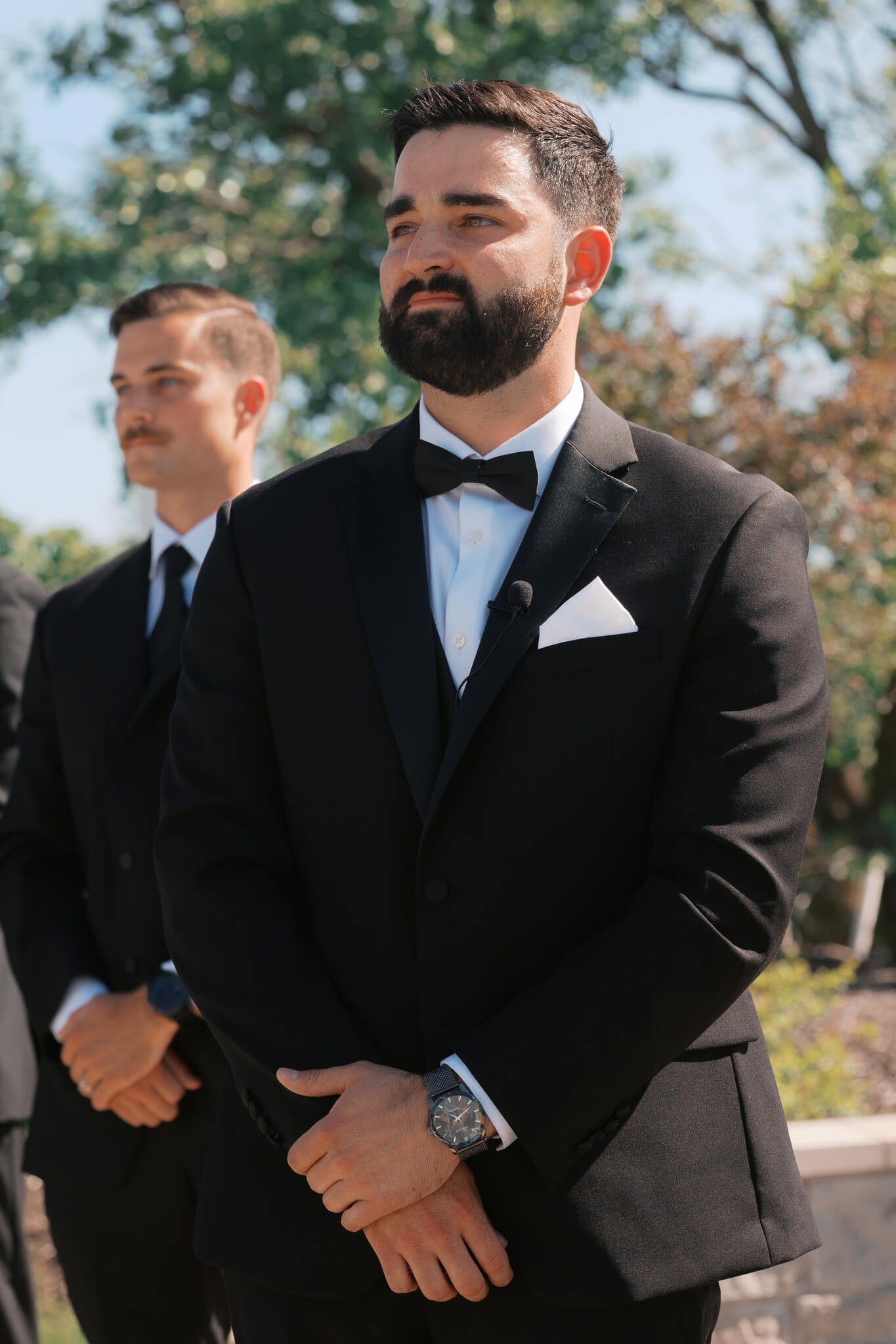 A groom happily awaits his bride in his black tux at the altar of his outdoor ceremony at The Acreage wedding venue