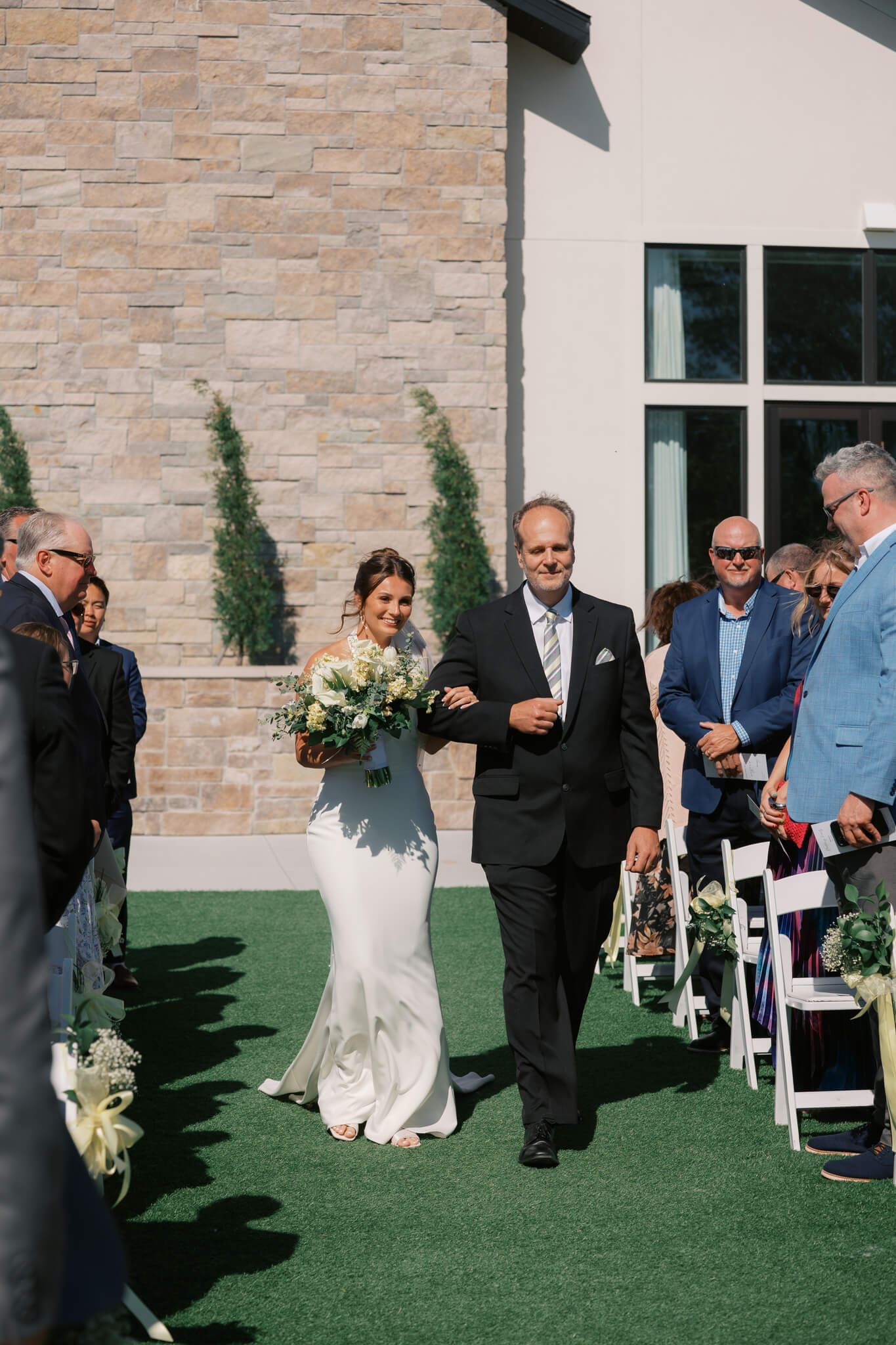 A happy dad in black walks with daughter down the aisle by the arm