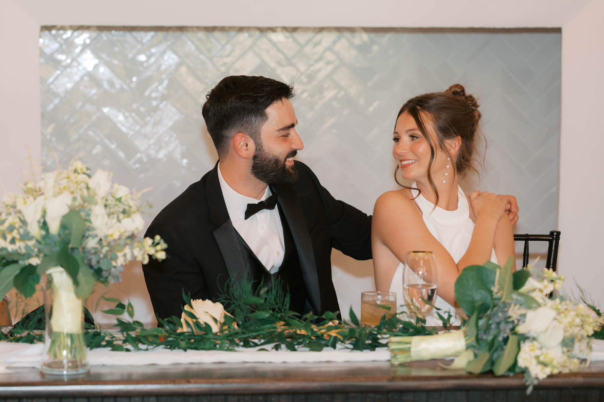 Newlyweds share a smile at each other while sitting at their head table at The Acreage wedding venue during their reception