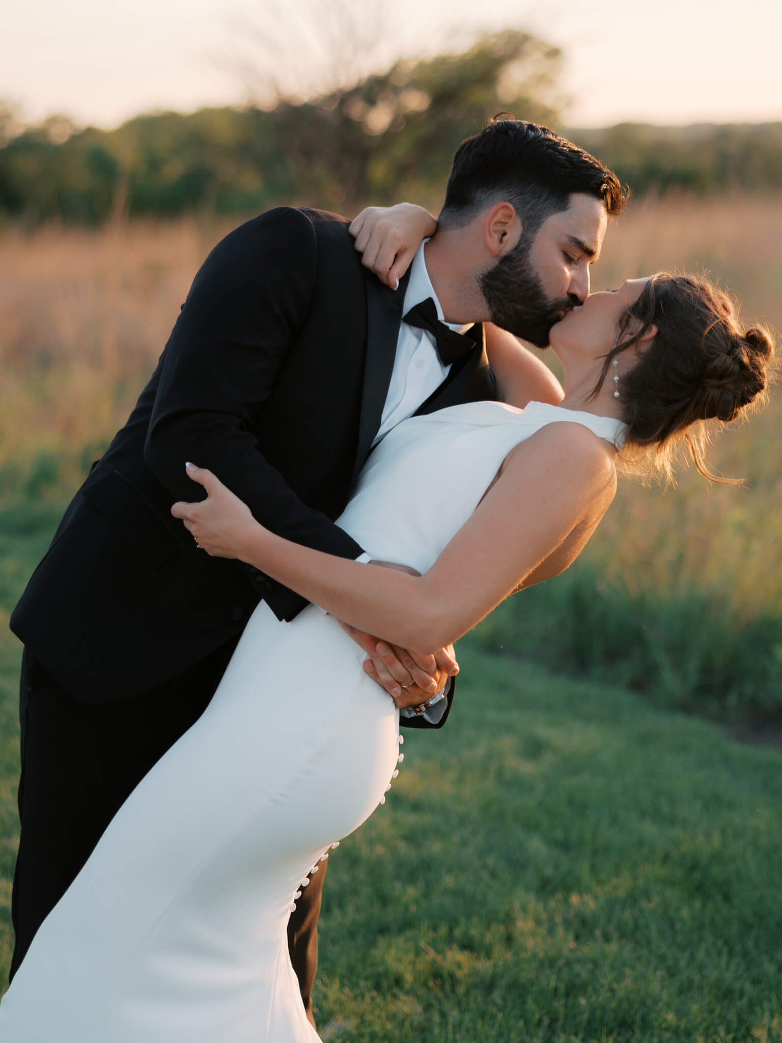 A groom dips and kisses his bride at sunset while enjoying the stunning view