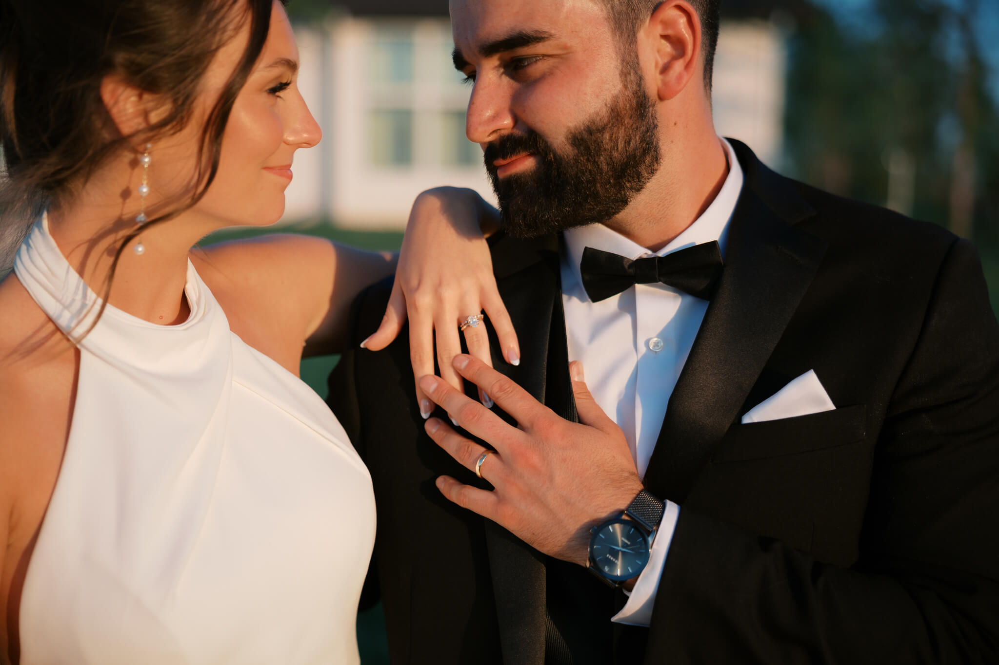 Details of a bride's ring hand on her groom's shoulder as he reaches up to touch it and they smile at each other