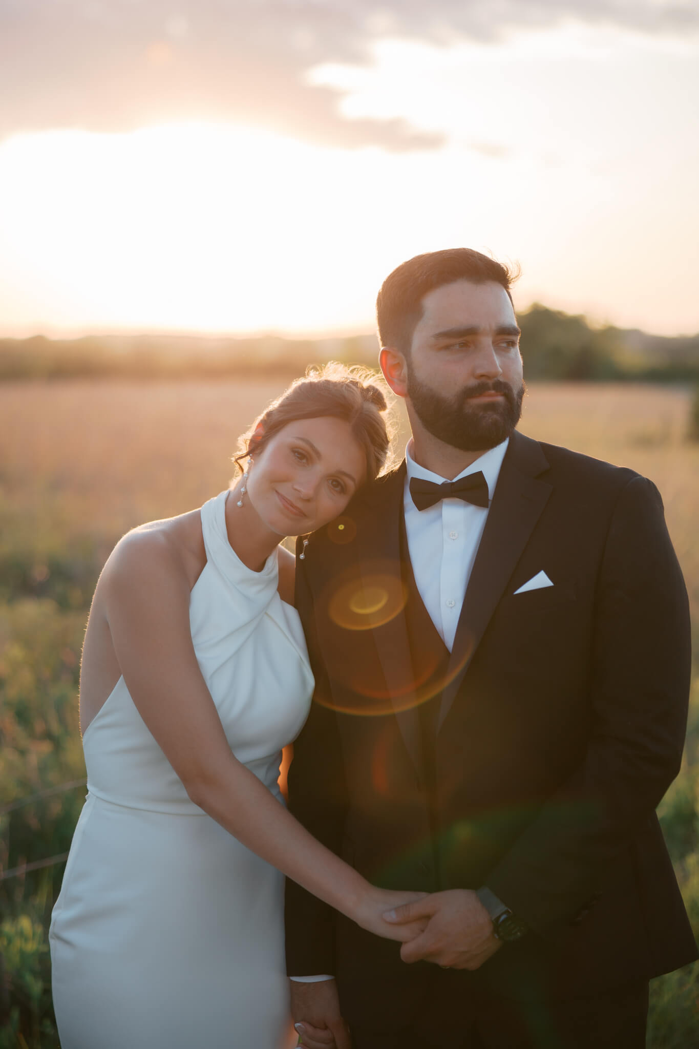 A bride rests her head on her groom's shoulder as they enjoy the sunset over the plains of The Acreage wedding venue