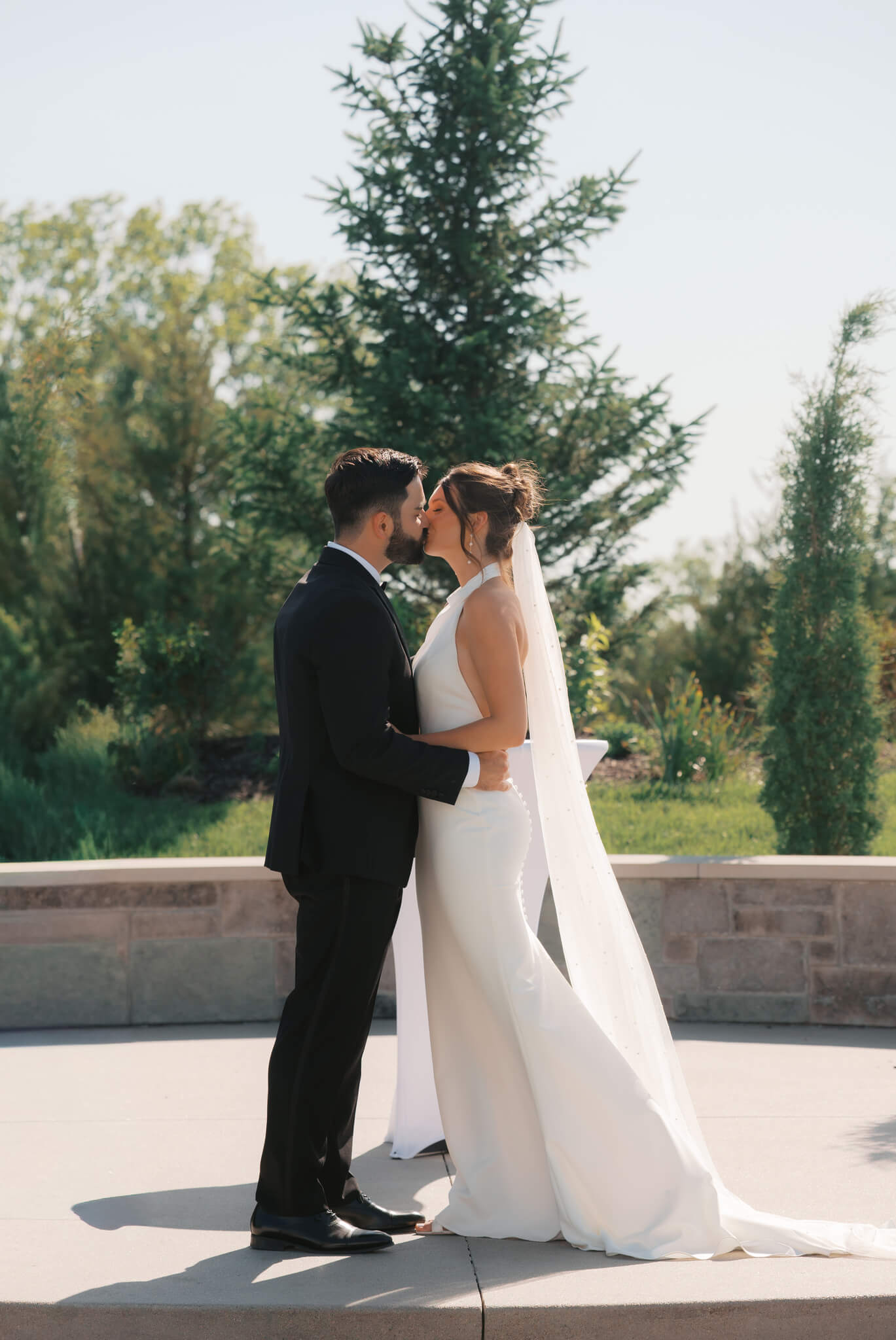 A bride and groom kiss on a platform in a garden to end their ceremony