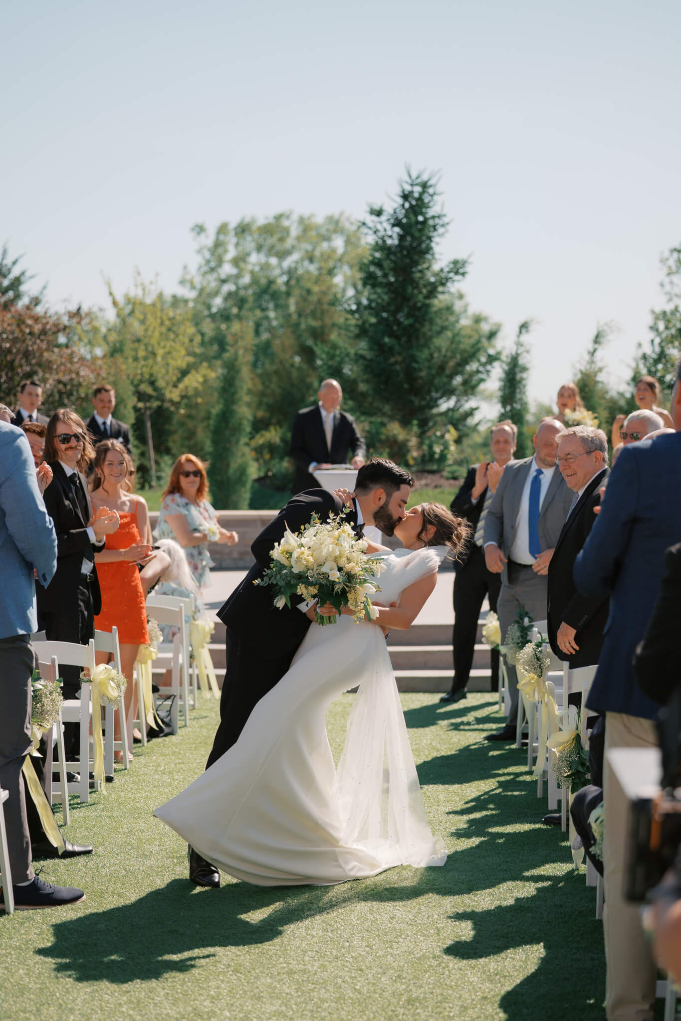 A bride is dipped and kissed in the aisle as guests watch to end an outdoor ceremony at The Acreage wedding venue