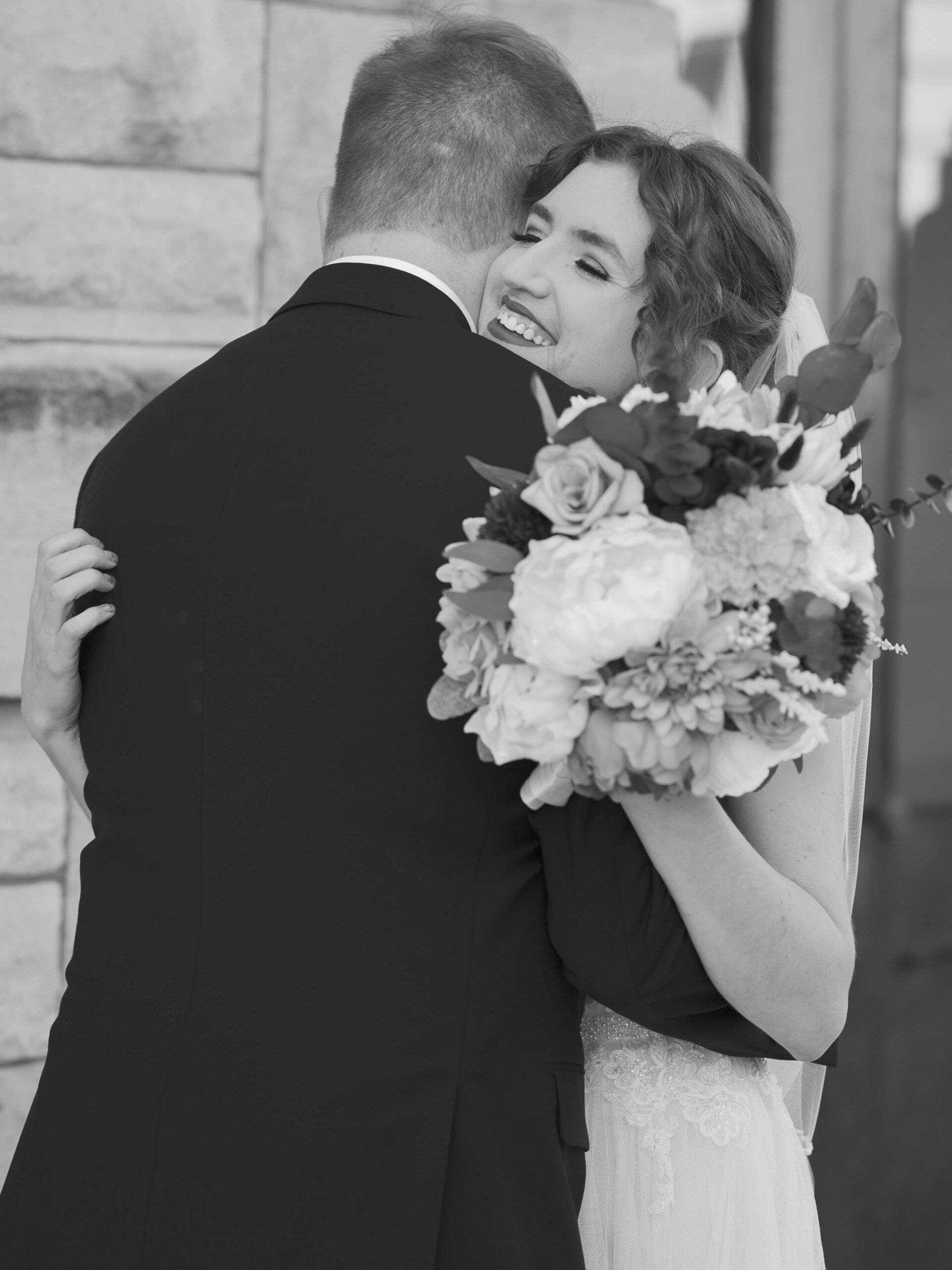 A happy bride hugs her groom while holding her bouquet during their empire room wedding