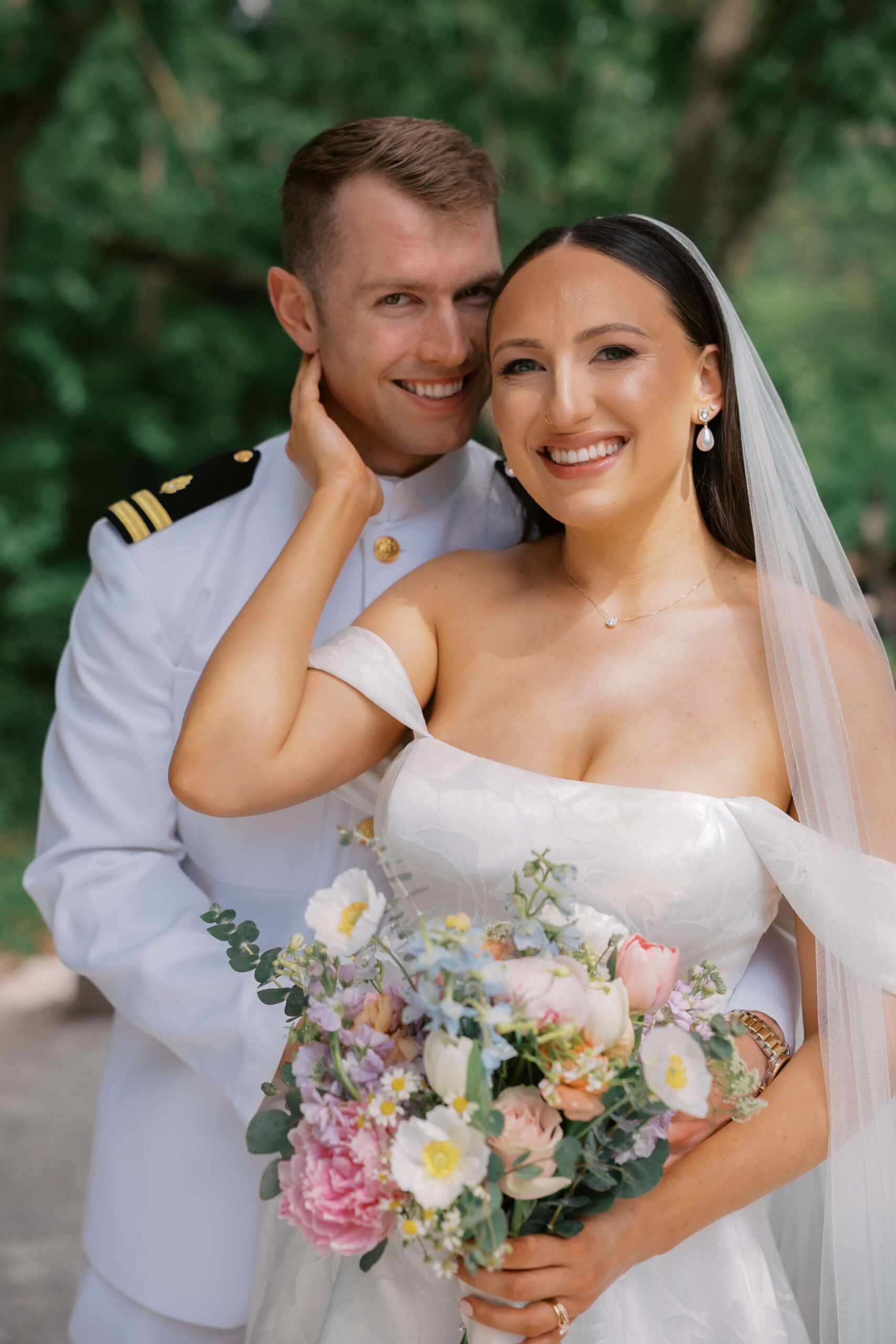 A bride and groom smile together while standing in the military white uniform with her hand on his cheek at their lauritzen gardens wedding
