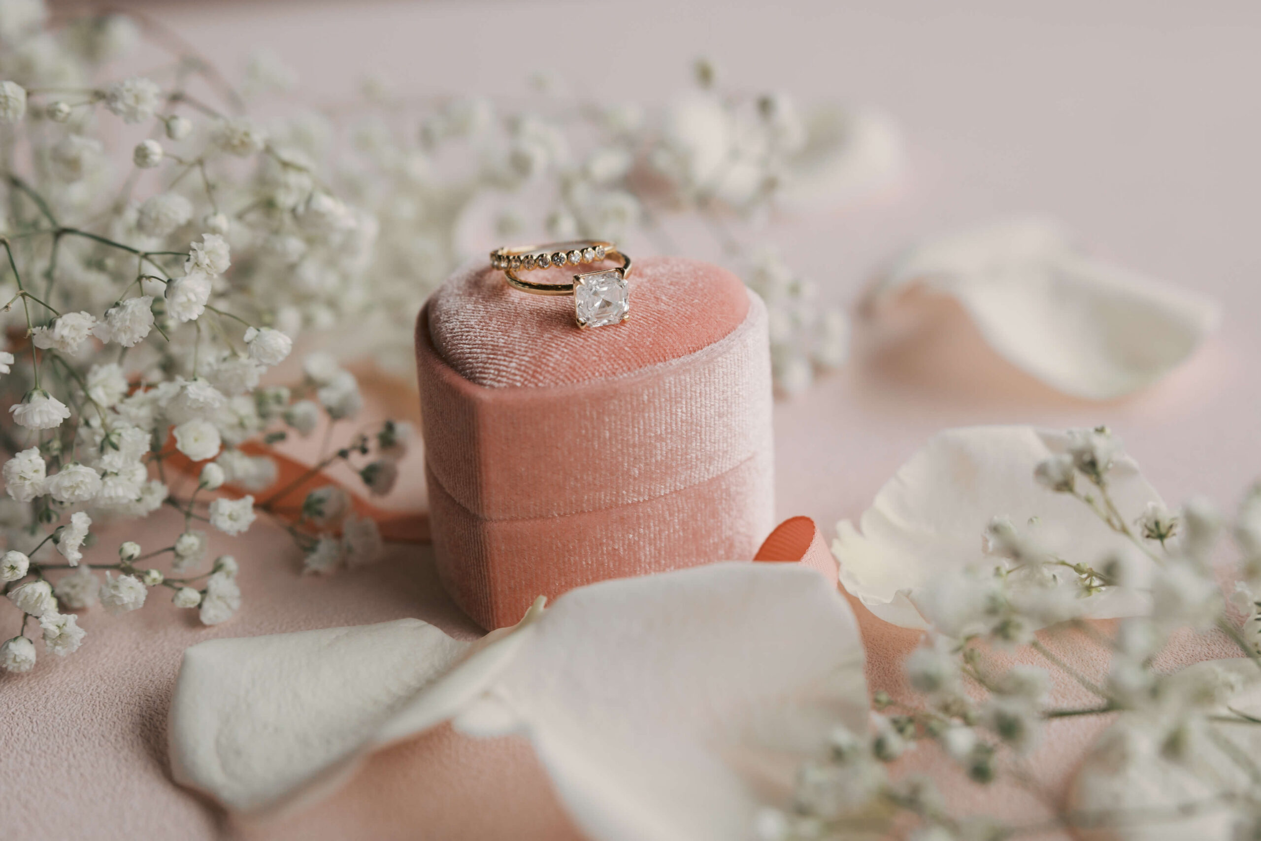 Details of wedding rings on a pink ring box surrounded by white flowers and petals at zenia omaha