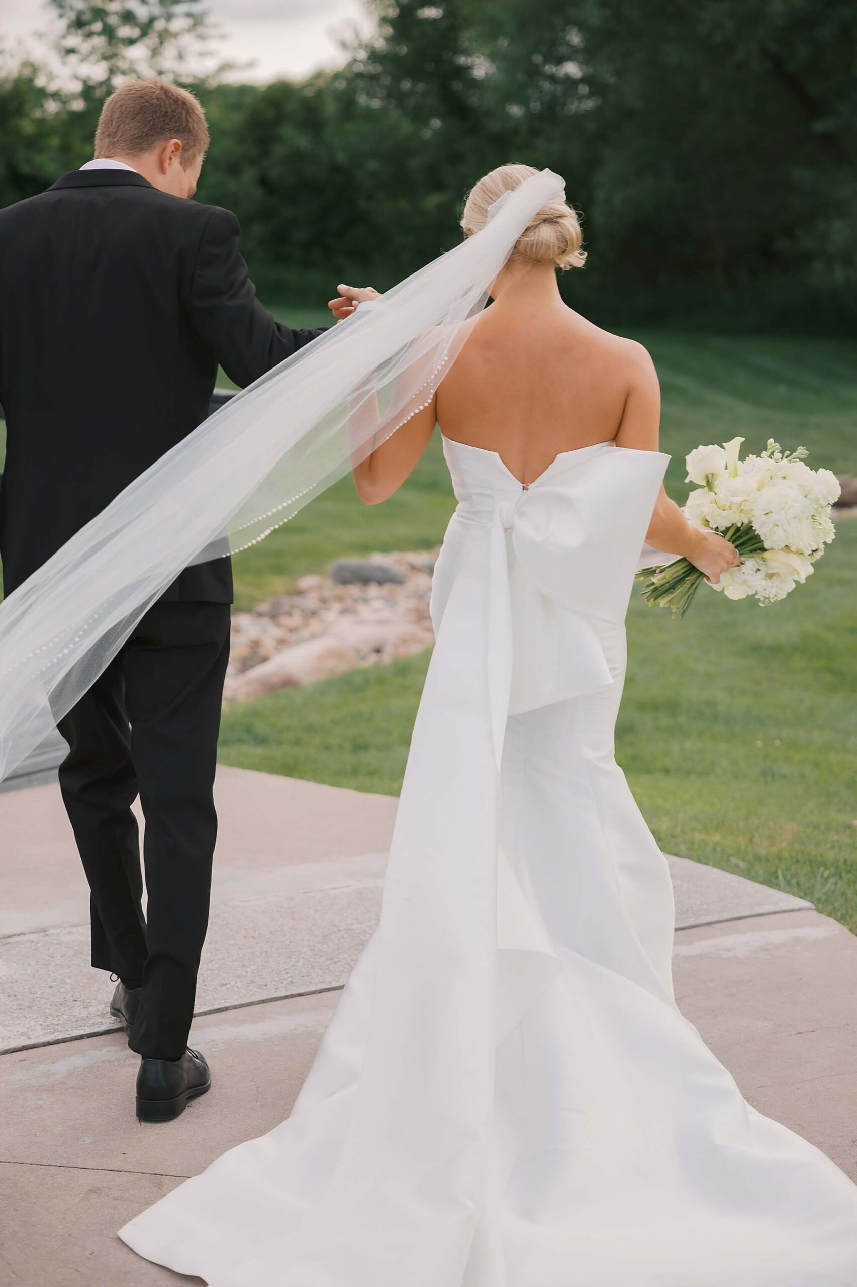 A bride walks holding hands with her groom on a sidewalk at sunset