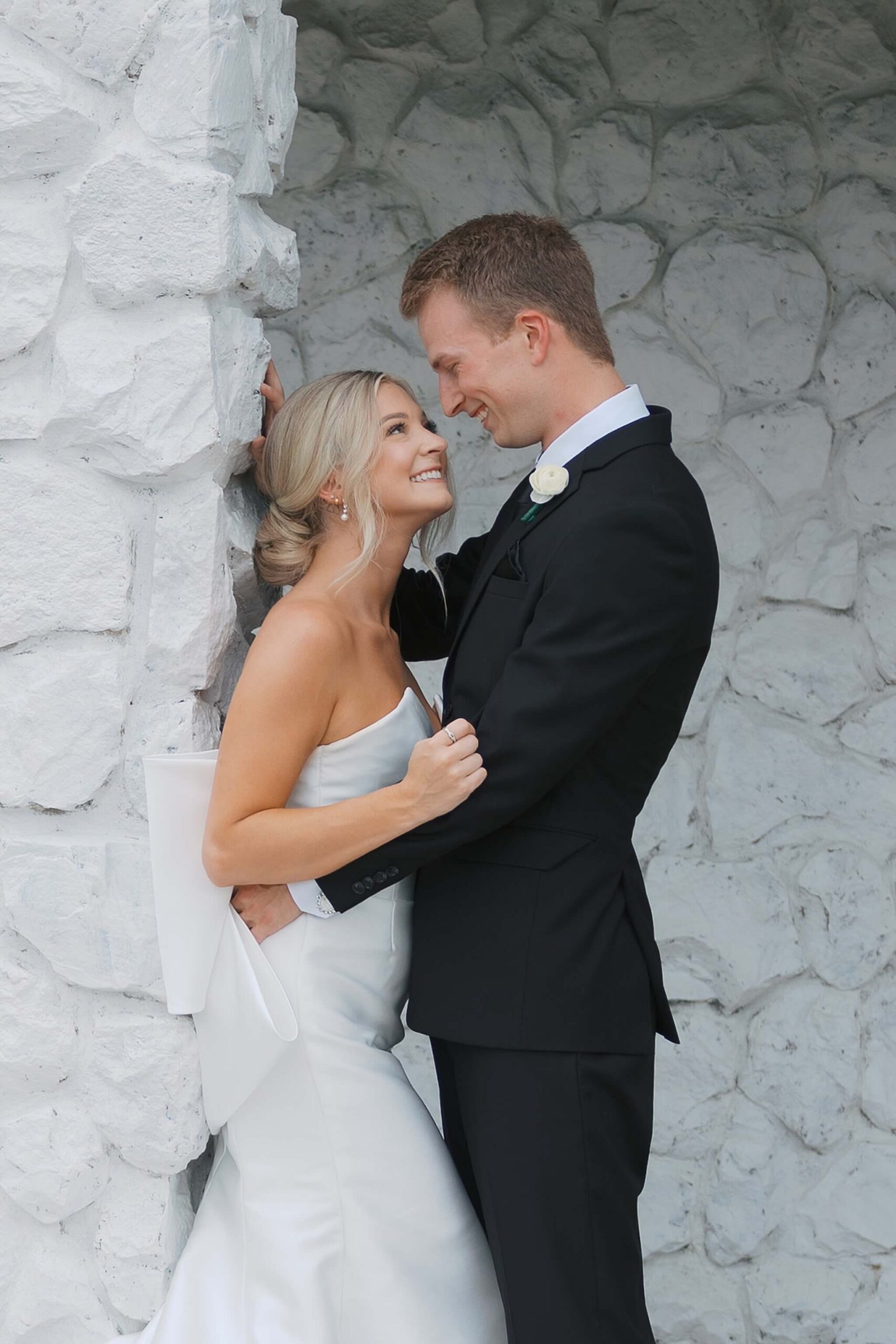 Newlyweds snuggle against white stone walls at The Fountains Ballroom wedding venue