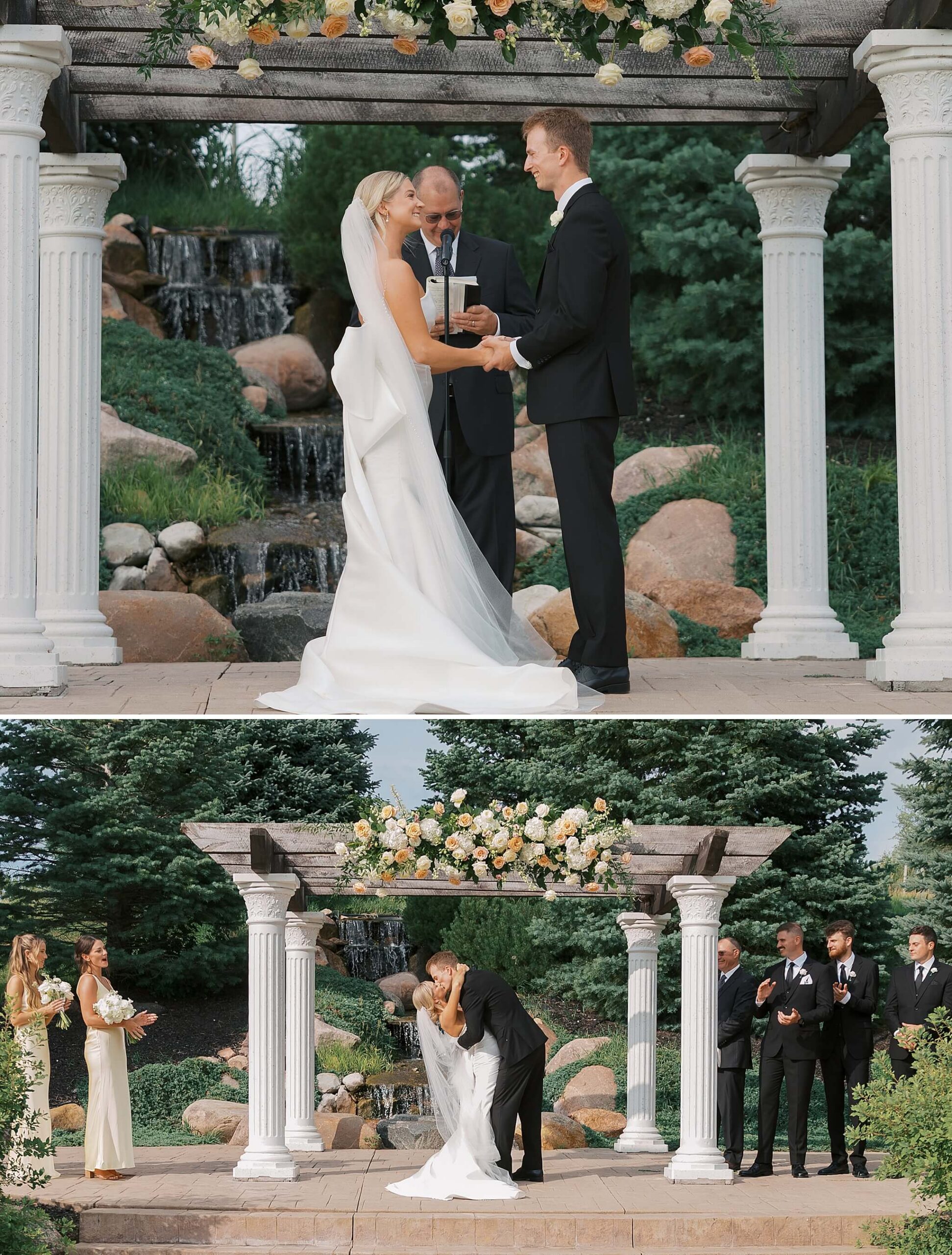 A bride and groom stand under an arbor in front of a garden waterfall at The Fountains Ballroom wedding venue during their ceremony holding hands and kissing