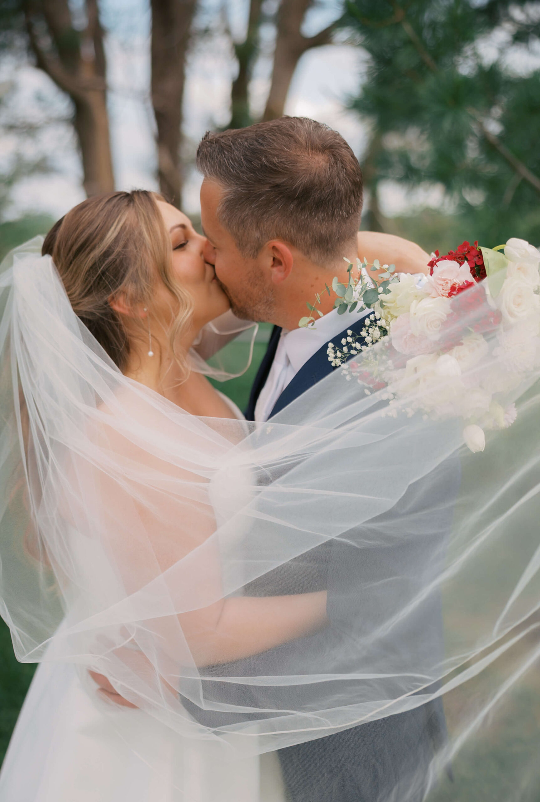 Newlyweds kiss while wrapped in the veil at sunset