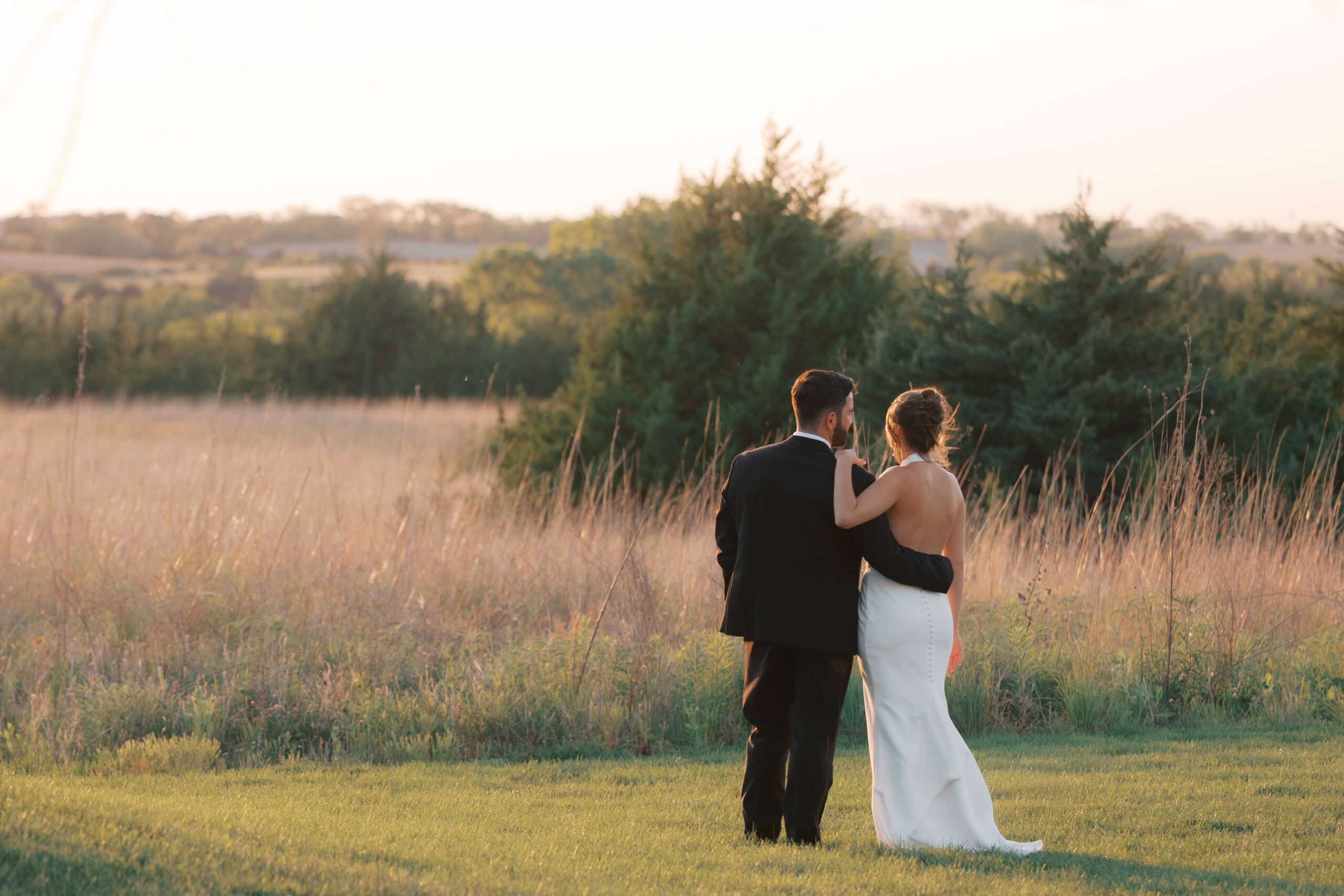 A bride and groom snuggle while watching the sunset over a valley