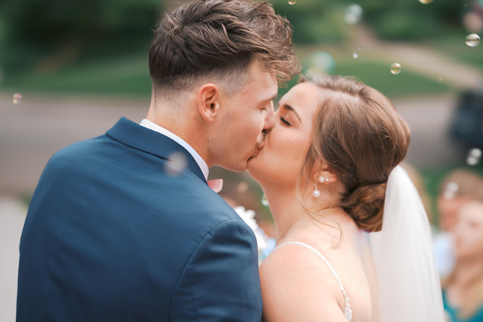 Newlyweds kiss while bubbles float around them